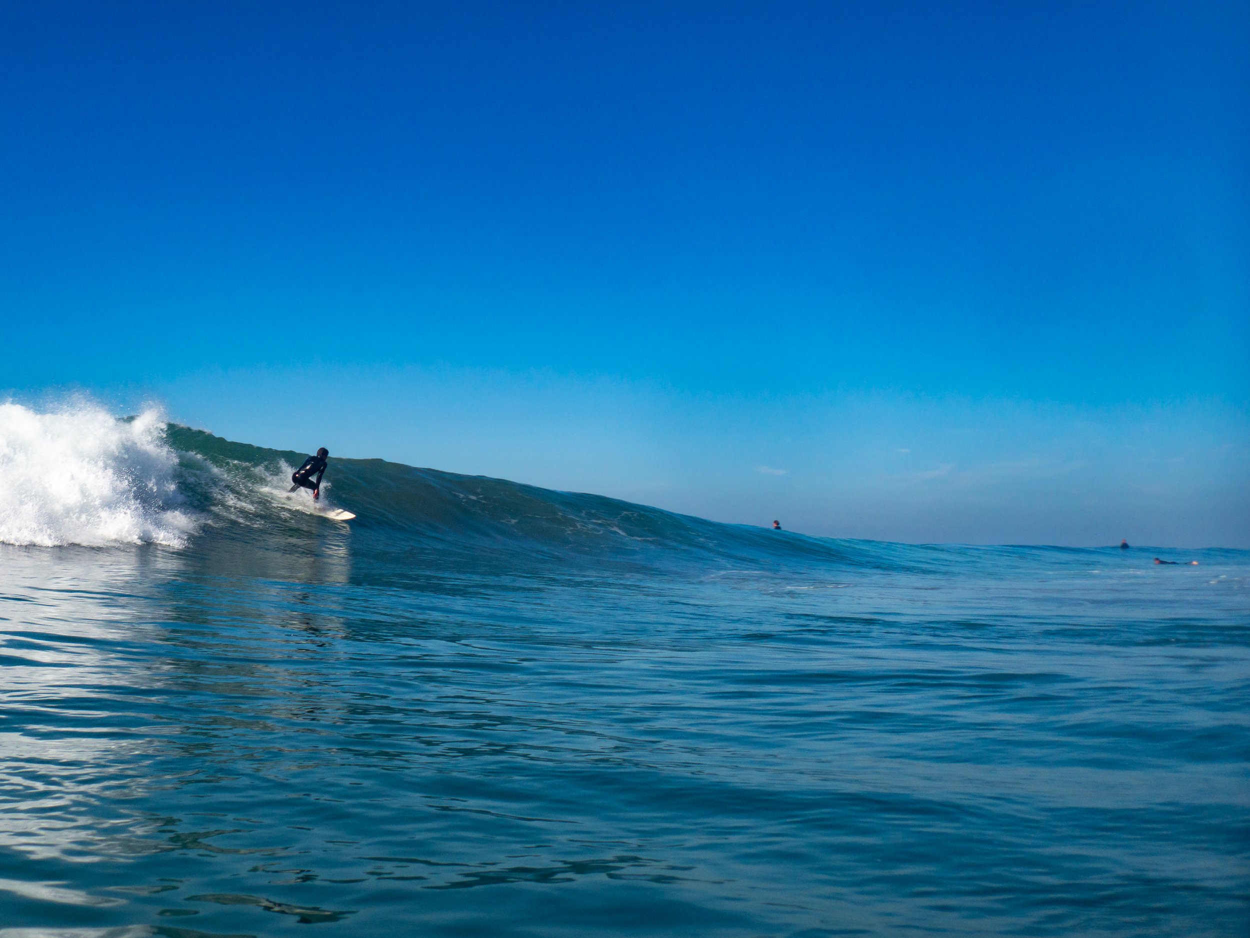 A person surfing on a large wave with a clear blue sky in the background.