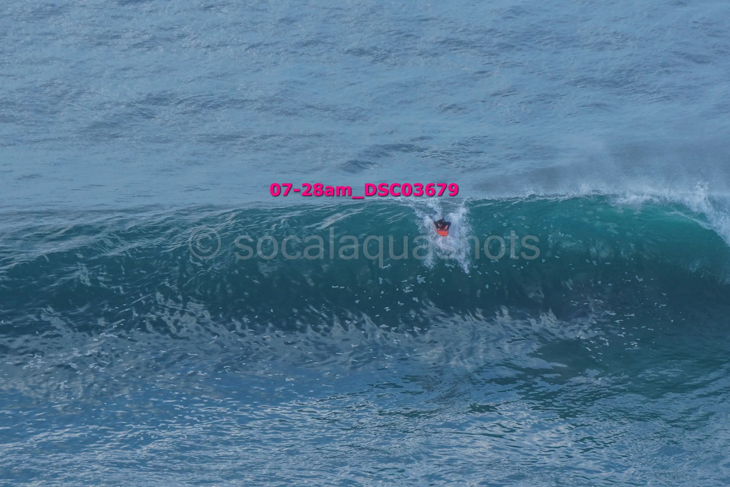 Person surfing on a wave in the ocean under a clear sky.