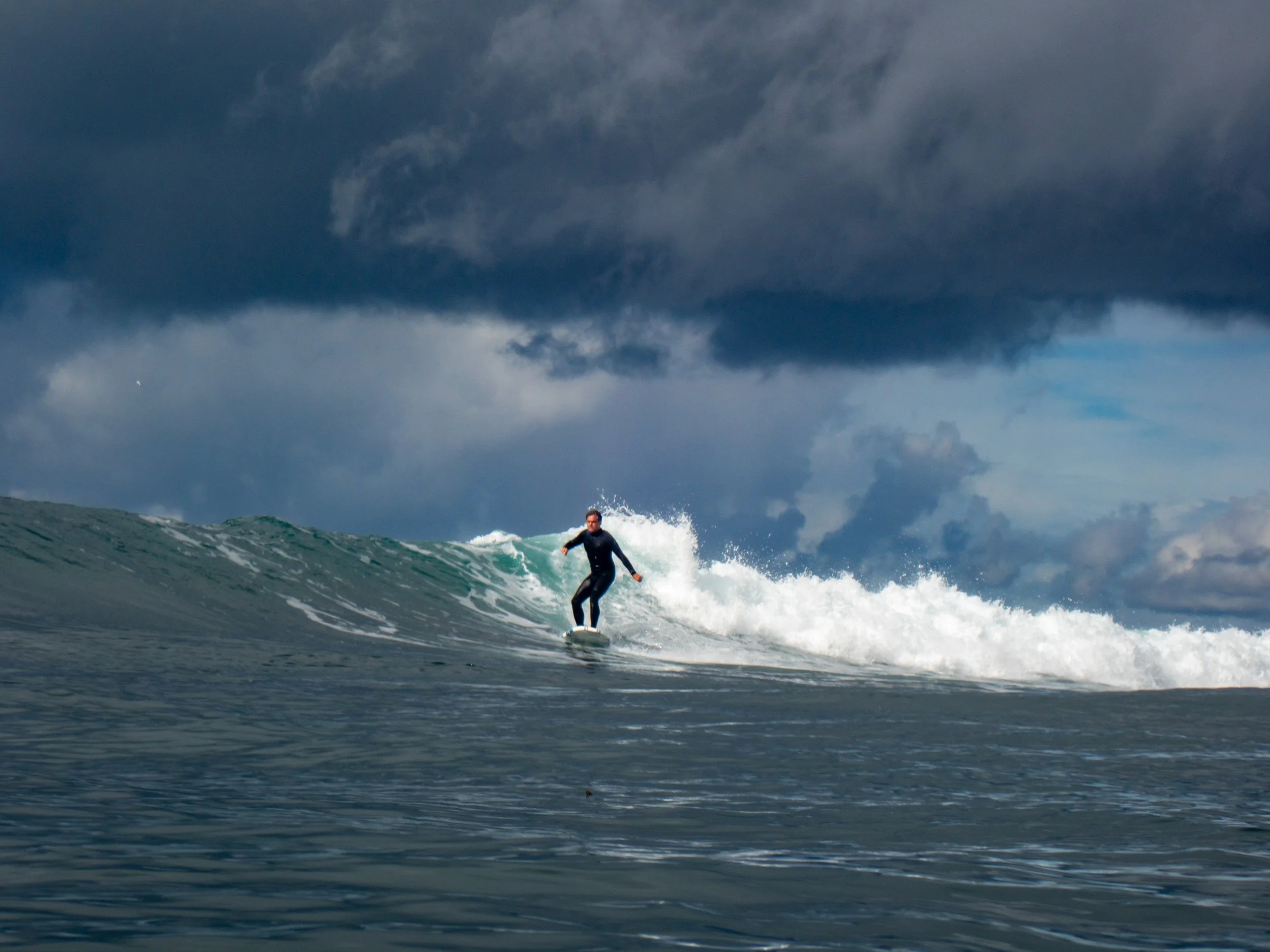 A person surfing on a wave in the ocean under a cloudy sky.