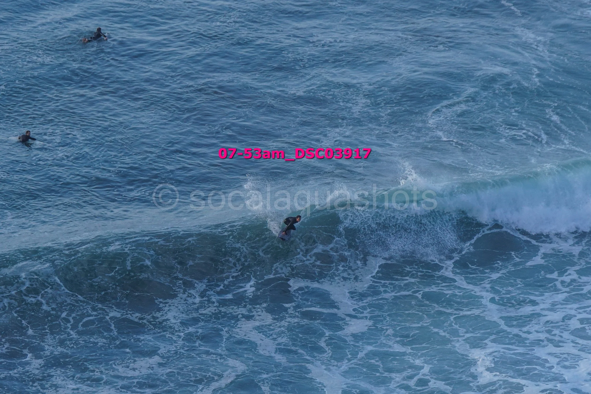 Surfer riding a wave in the ocean with three other people swimming or surfing in the background.
