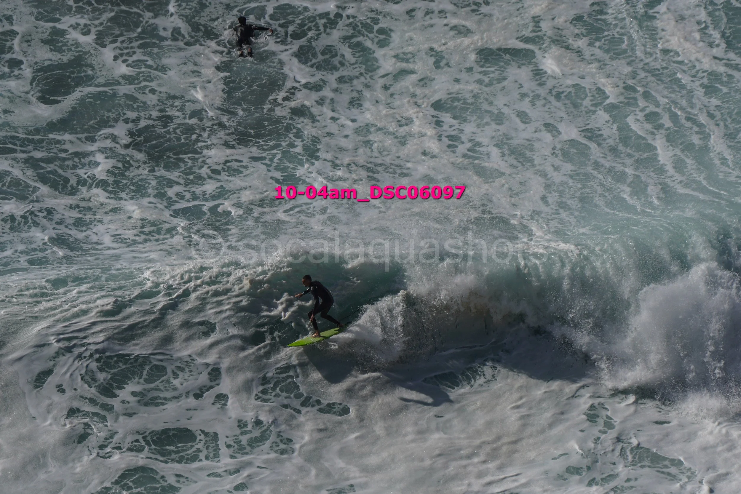 A surfer riding a wave while another person is further in the water, with the ocean's waves and foam around them.