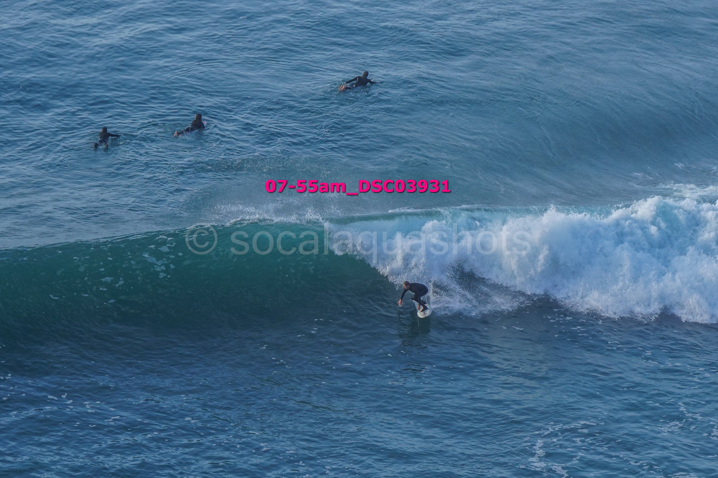 A person surfing on a wave with three surfers in the water nearby.