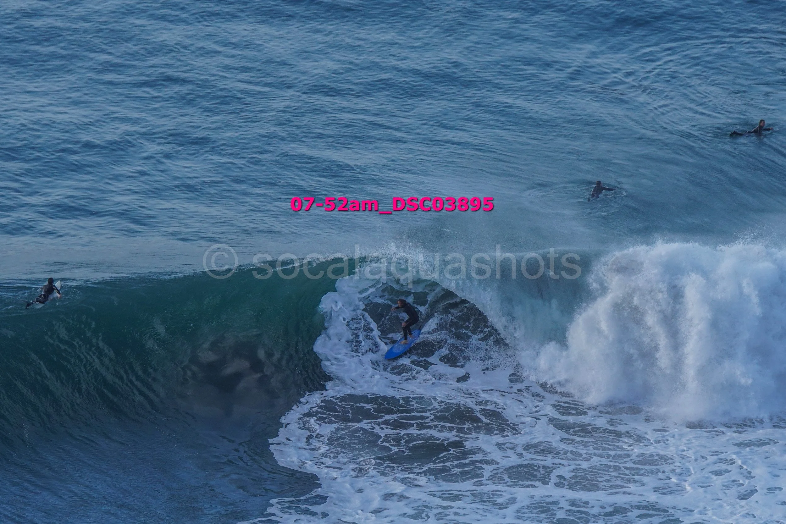 Surfer riding a large wave with three other surfers in the water watching.