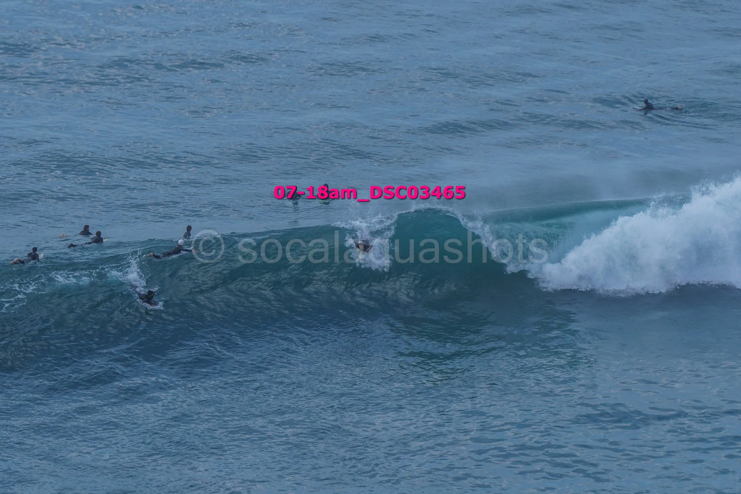 Several surfers riding and waiting for waves in the ocean with a wave breaking in the foreground.