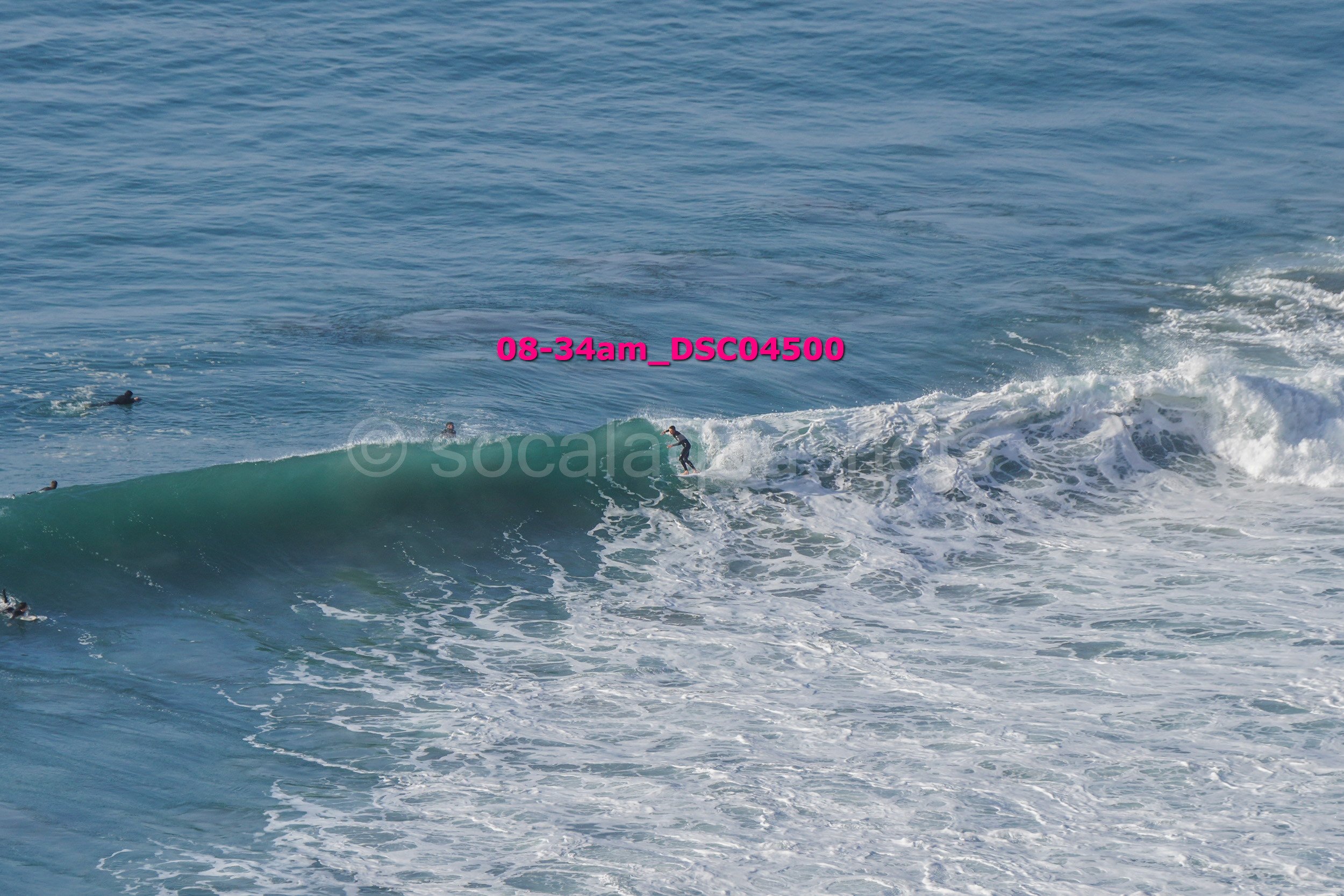 Surfer riding a wave in the ocean with several other surfers in the water nearby.