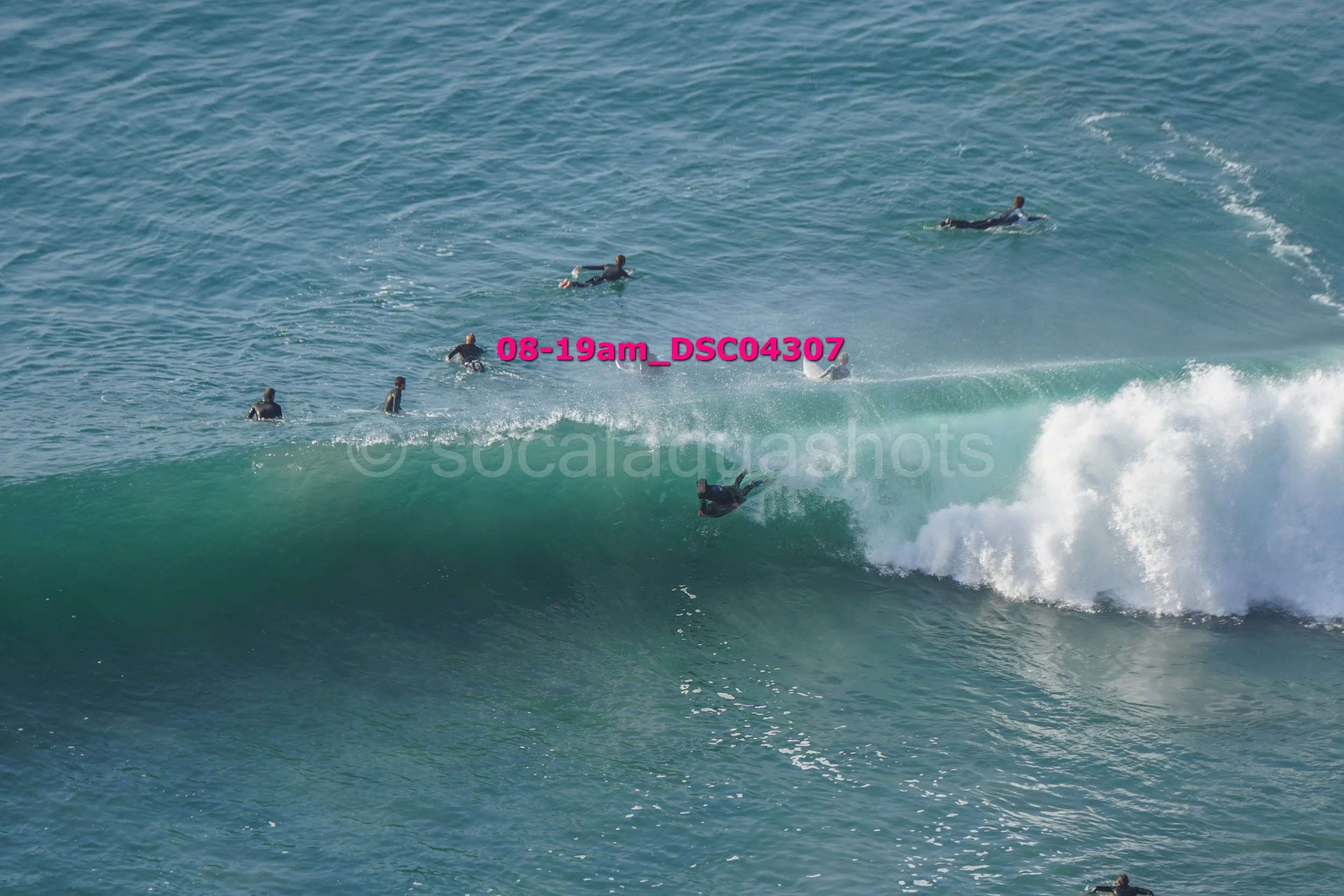 A person surfing on a wave with several other surfers in the water nearby.