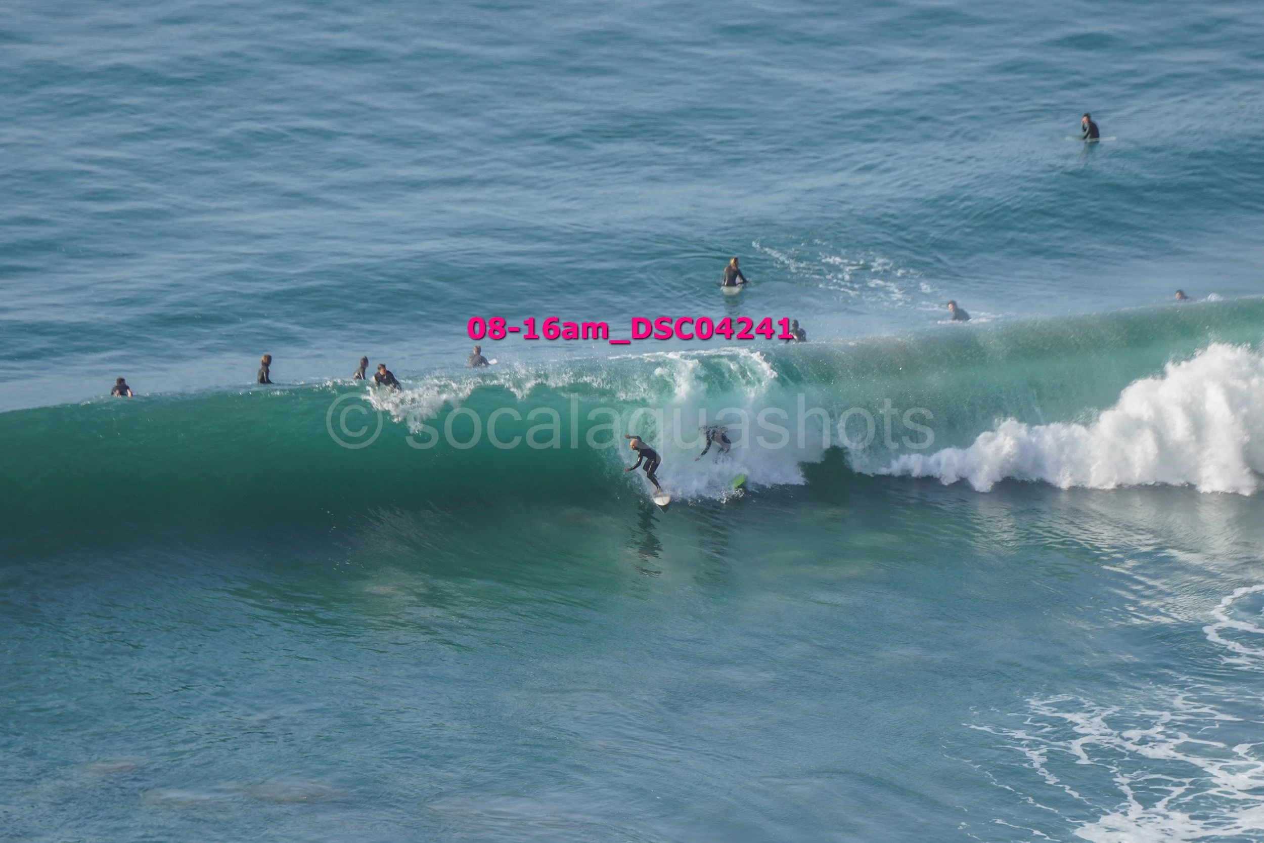 A group of surfers in wetsuits riding and waiting on ocean waves