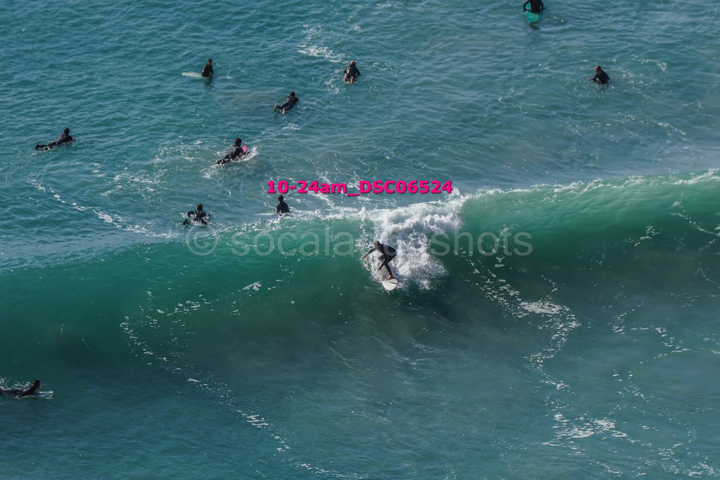 Surfer riding a wave with multiple people swimming and surfing in the background in the ocean.