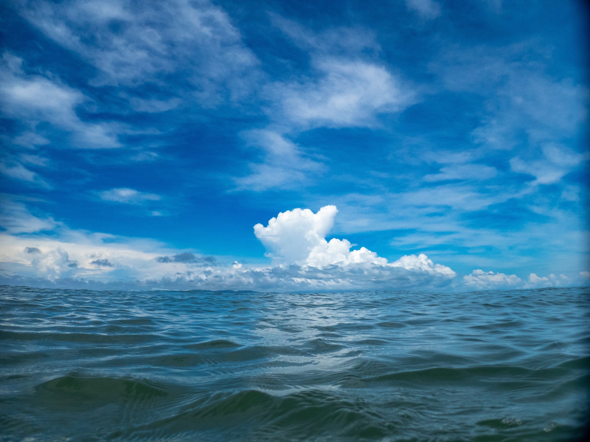 Open ocean under a partly cloudy blue sky.