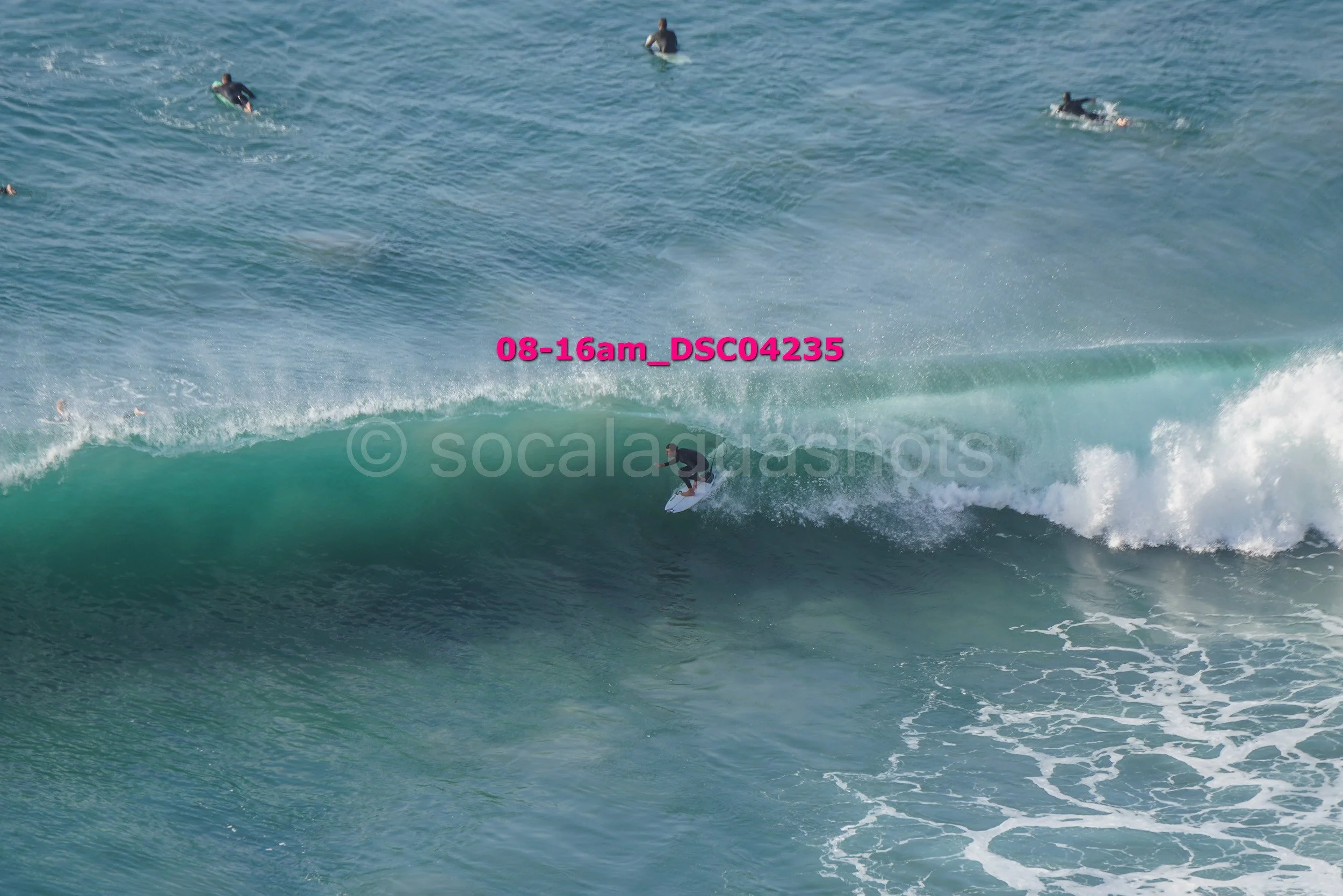 Surfer riding a wave in the ocean with several people swimming in the background.