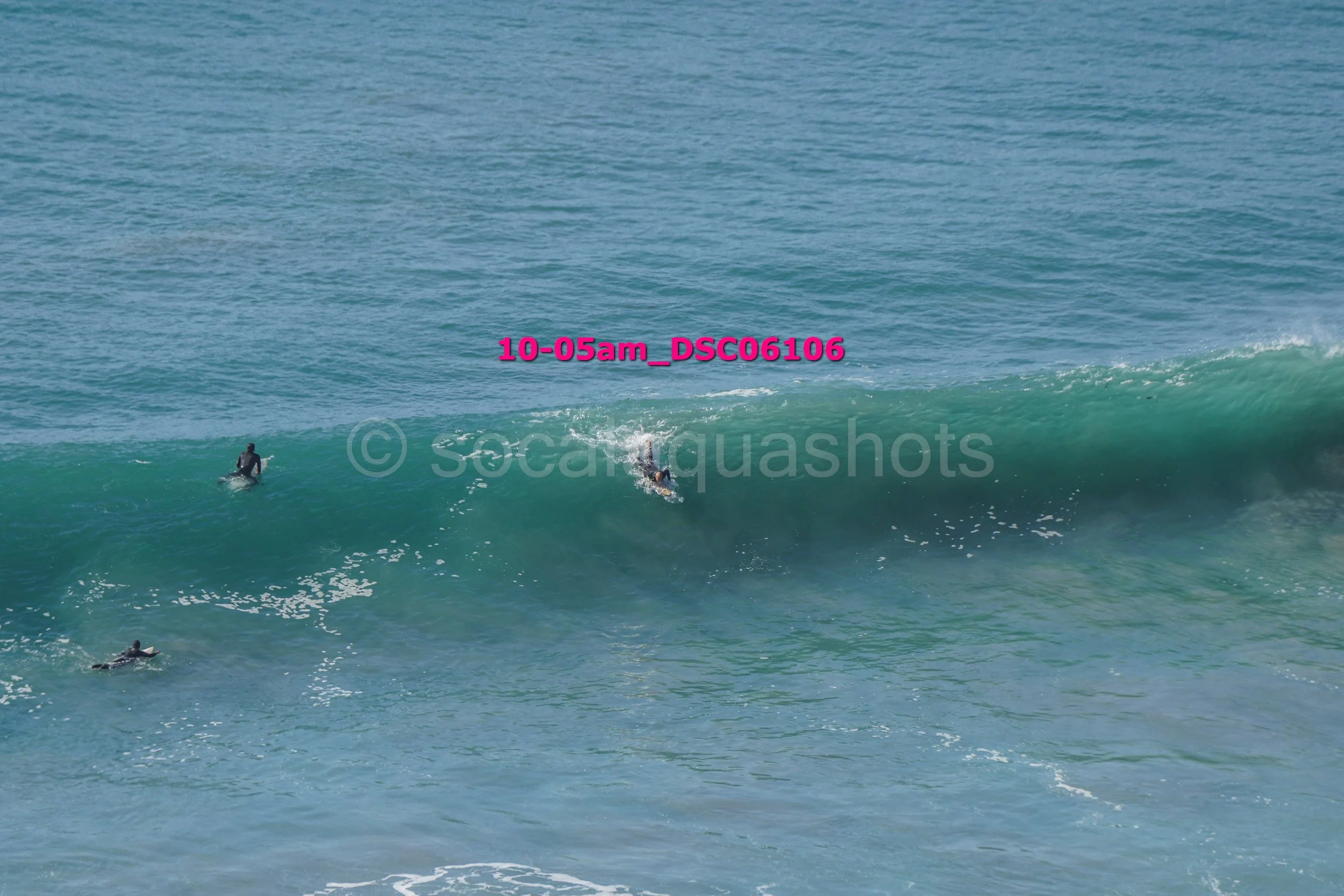 Three surfers in wetsuits riding and waiting for waves in the ocean.
