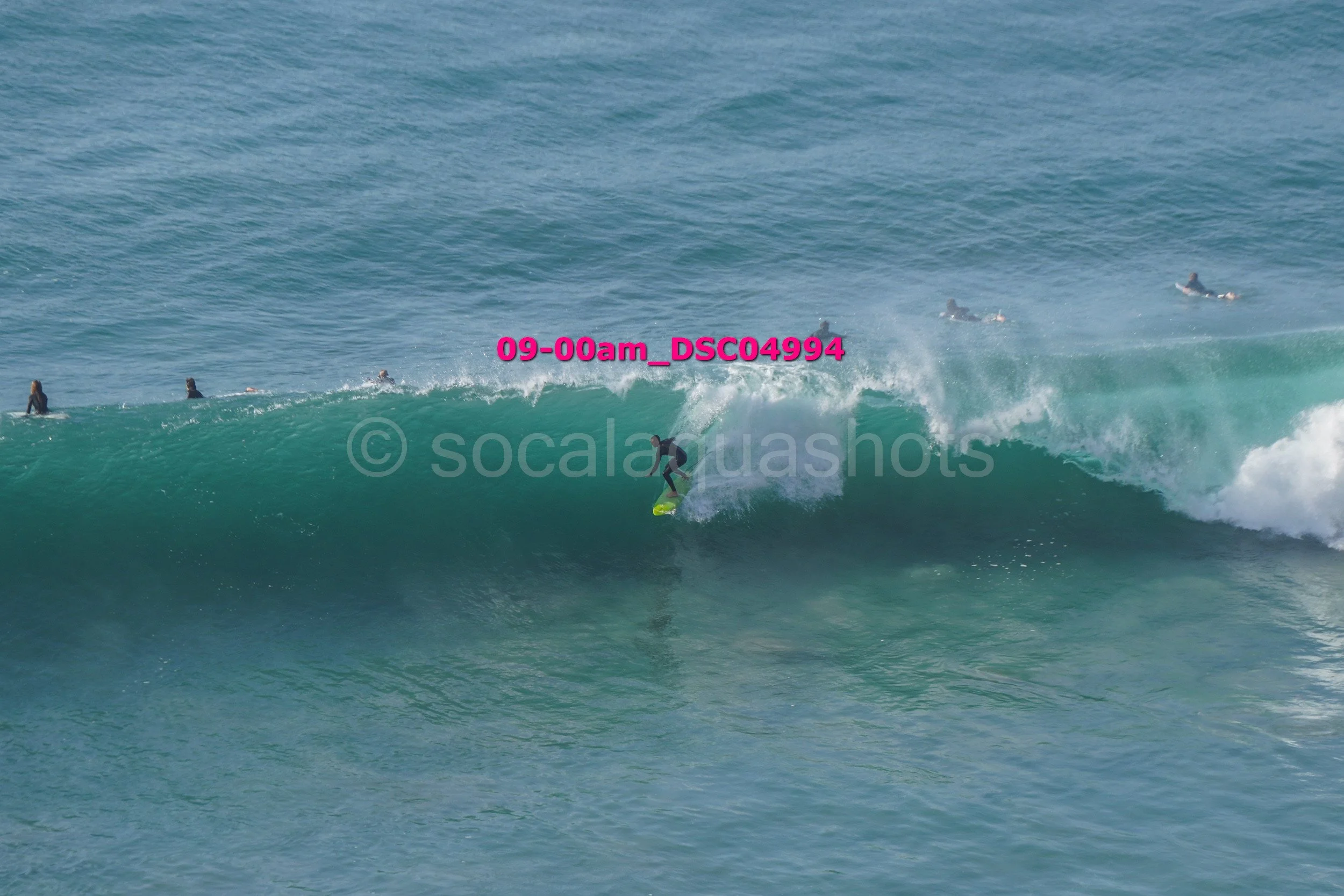 A surfer riding a large wave with multiple surfers in the background in the ocean.