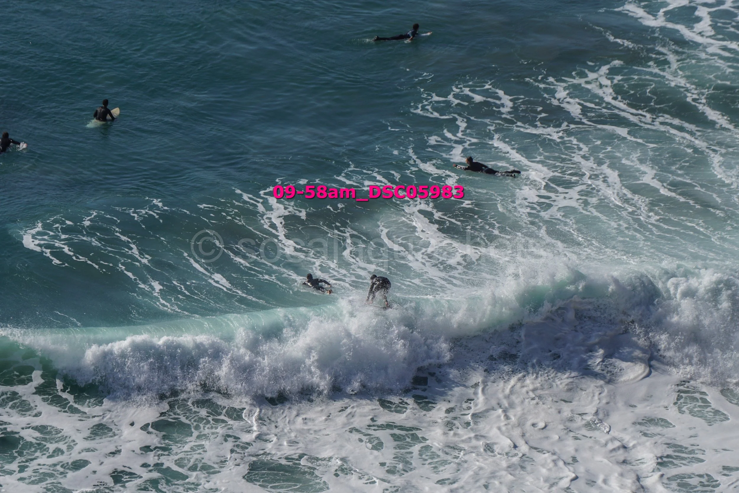 Several surfers in the ocean riding and paddling on surfboards among crashing waves.