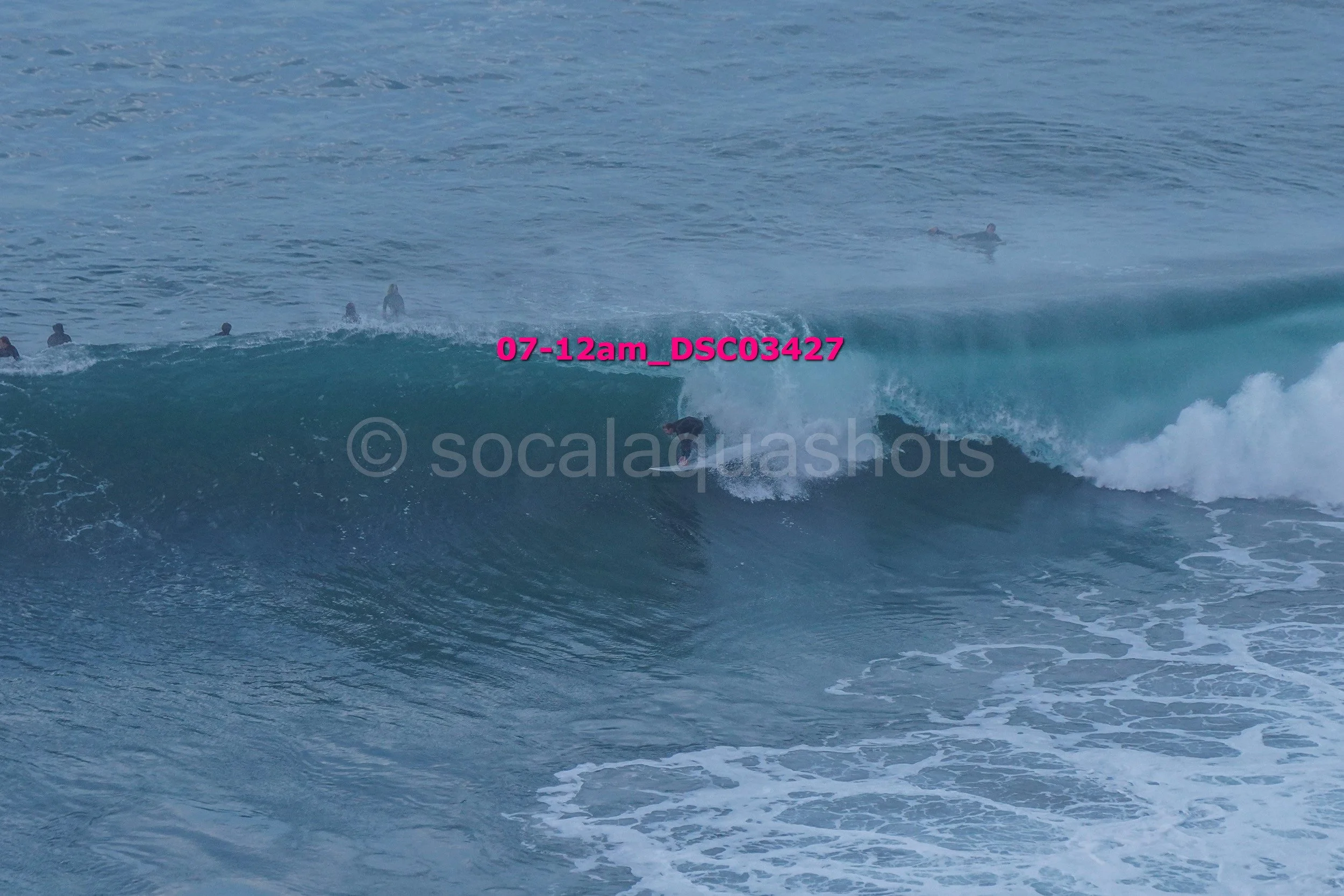A person surfing on a large wave in the ocean with several other surfers in the water in the background.