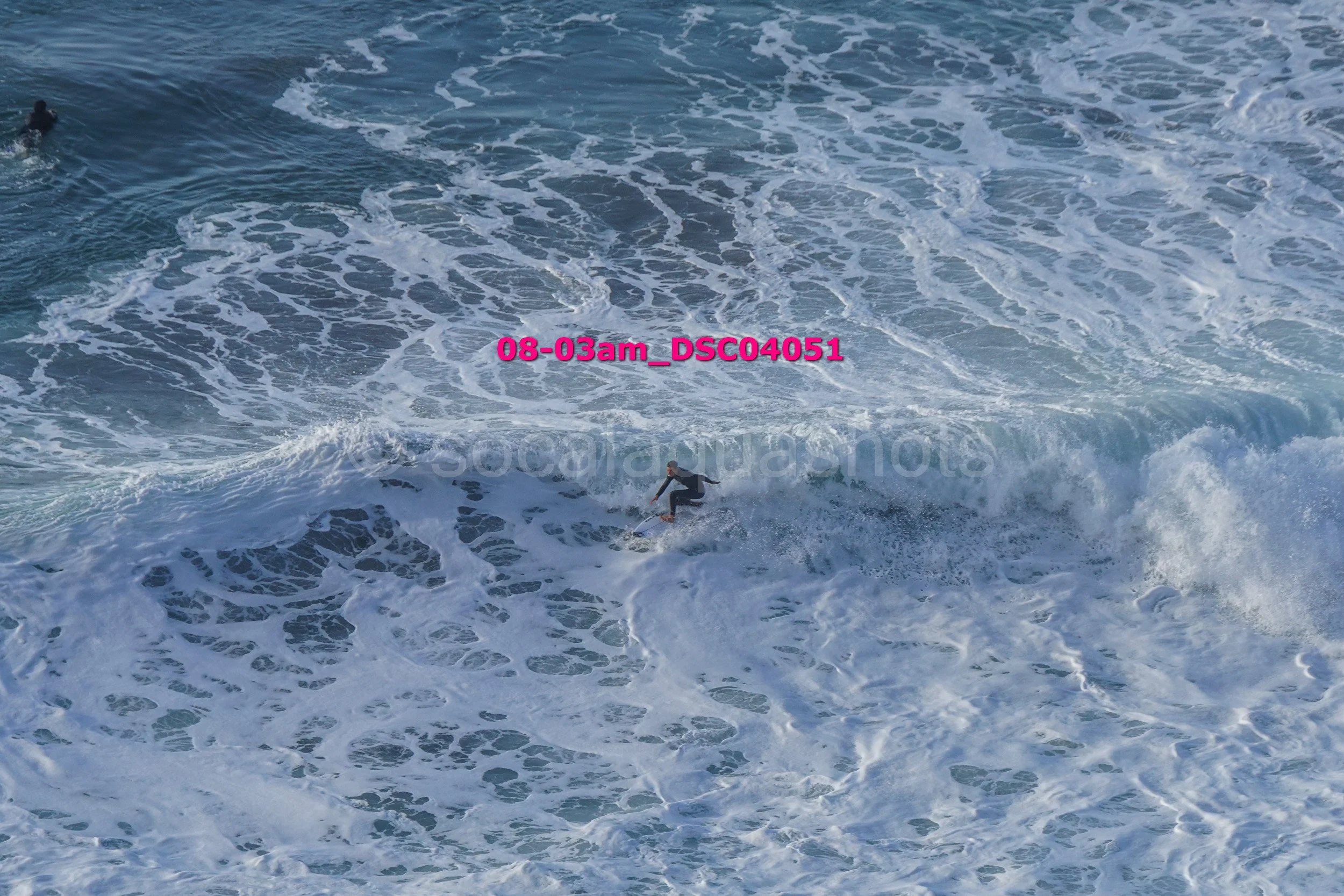 A person surfing on a wave in the ocean with other surfers visible in the background.