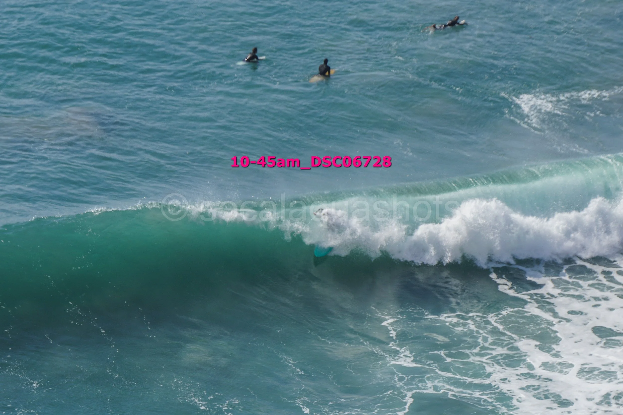 Surfer in turquoise wetsuit riding a wave, with four people paddling in the background in the ocean.