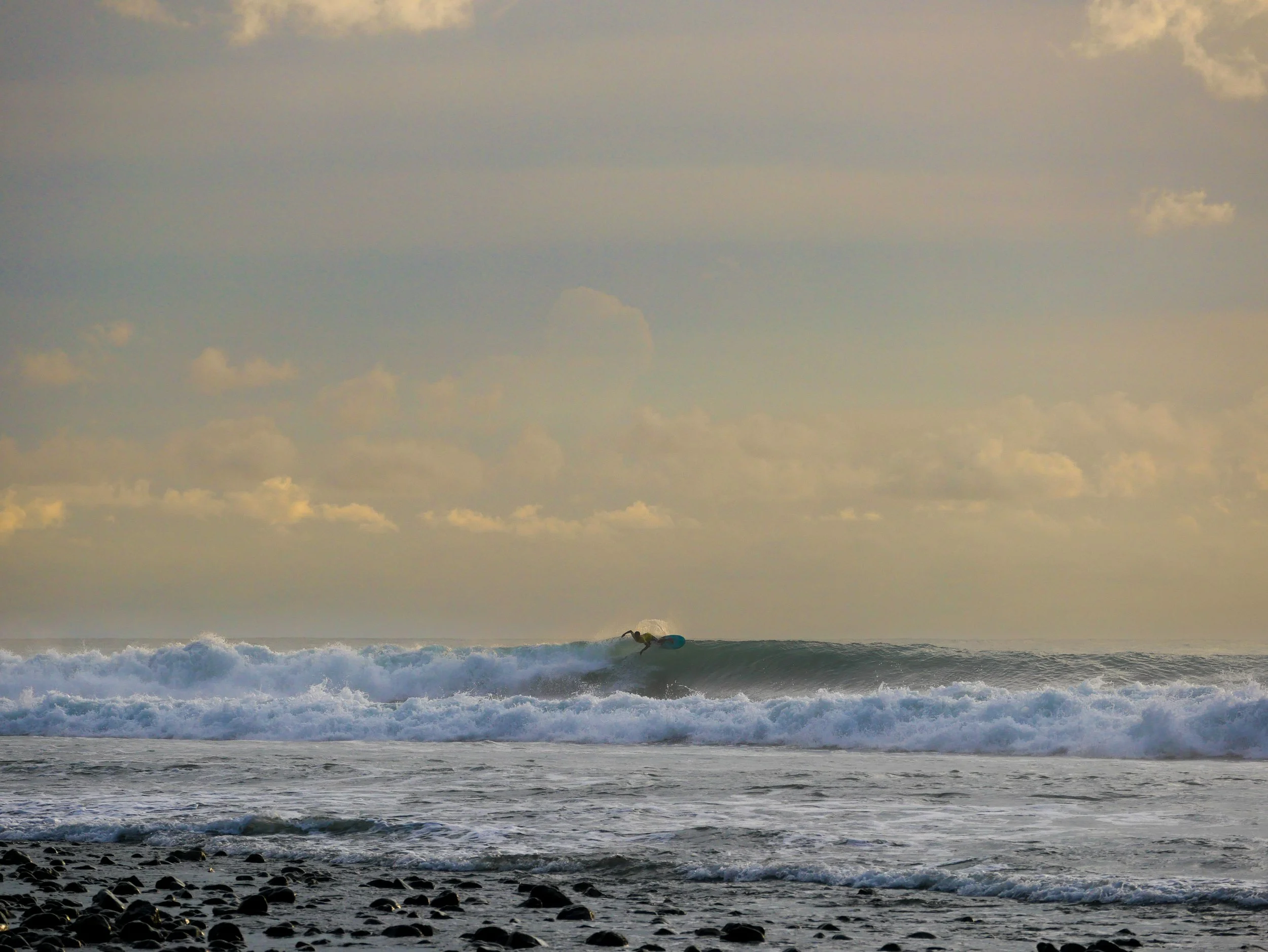 Surfer riding a wave at sunset with rocky shoreline