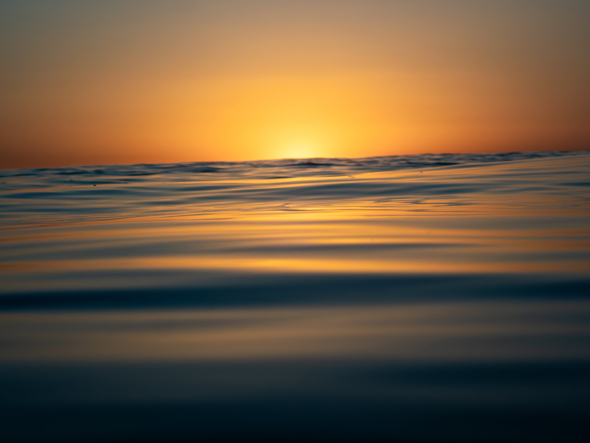 Sunset over the ocean with calm waves and a sky transitioning from orange to darker shades.