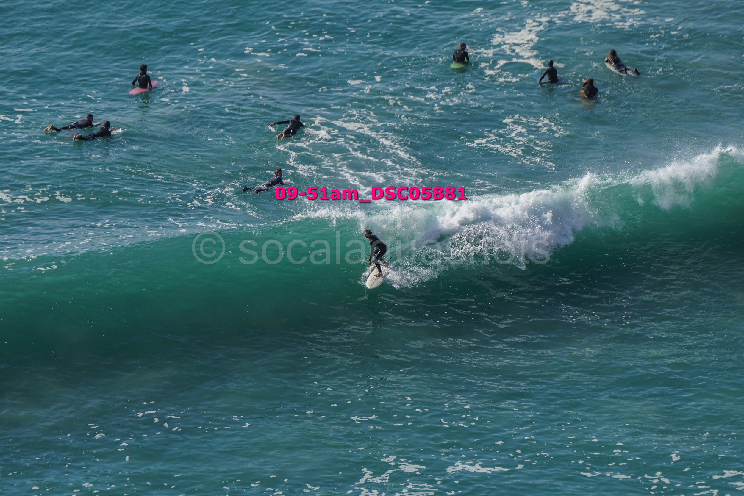 A person surfing on a wave with several people swimming and surfing in the background in the ocean.