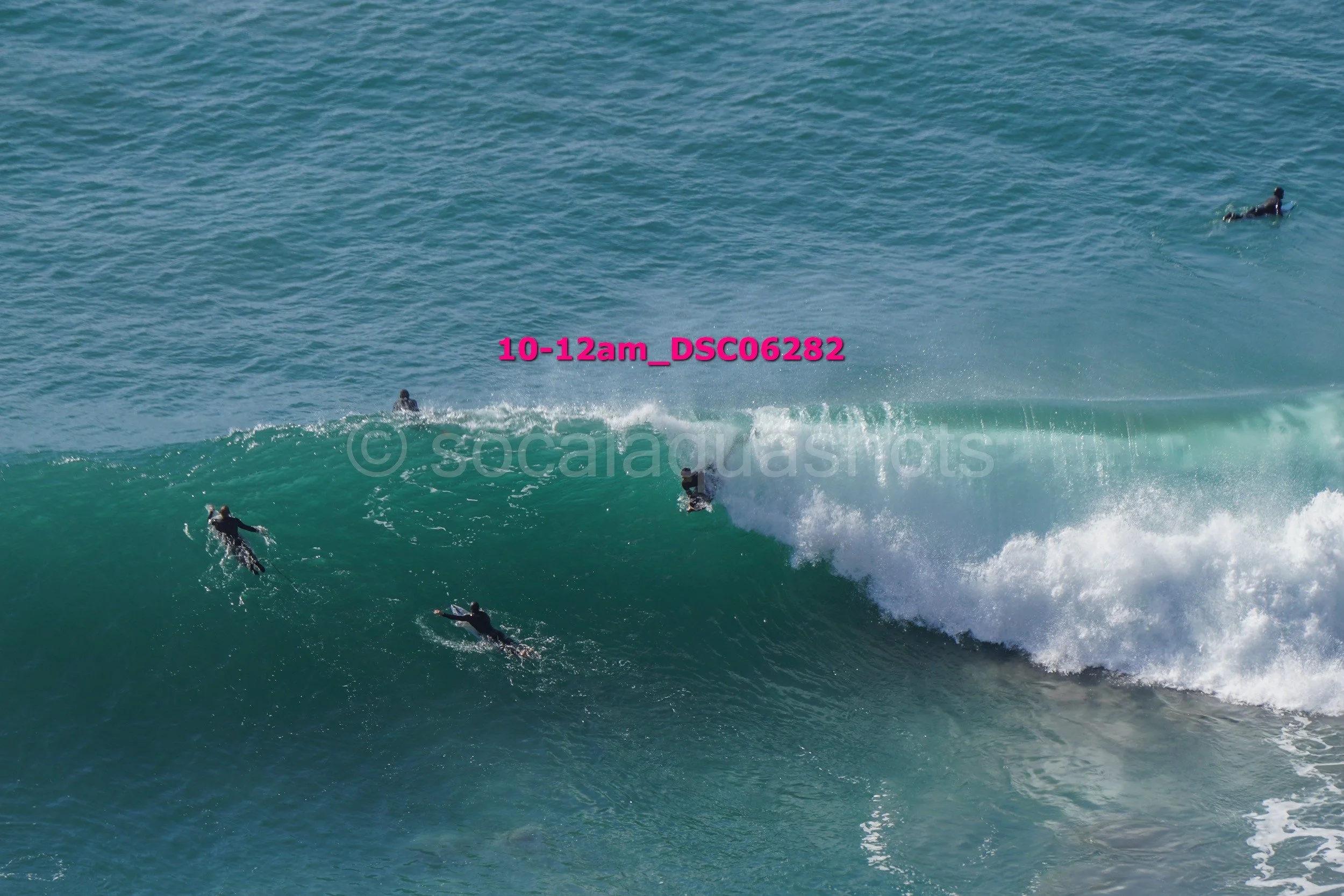 Surfers riding a large wave in the ocean, with some surfers already on the wave and others paddling to catch it.