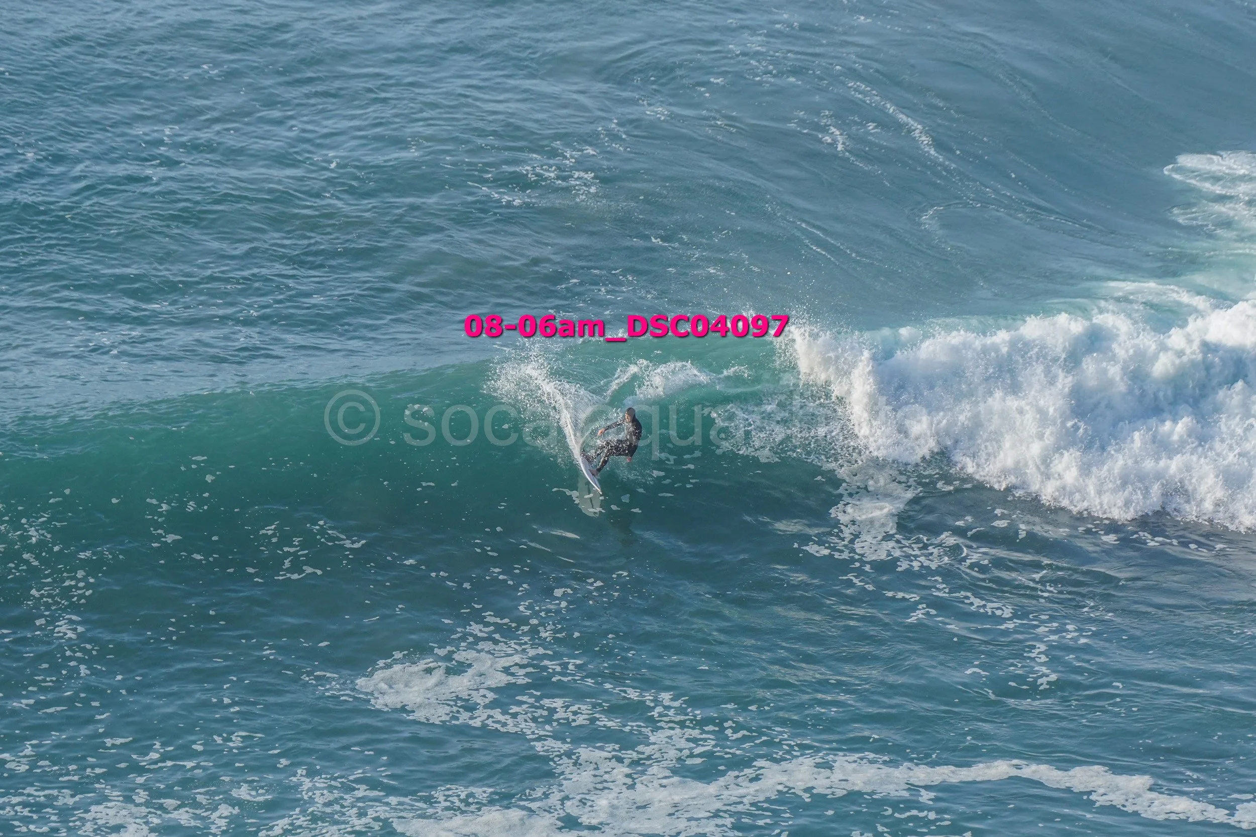 A person surfing on a wave in the ocean, wearing a black wetsuit, with water splashing around them.