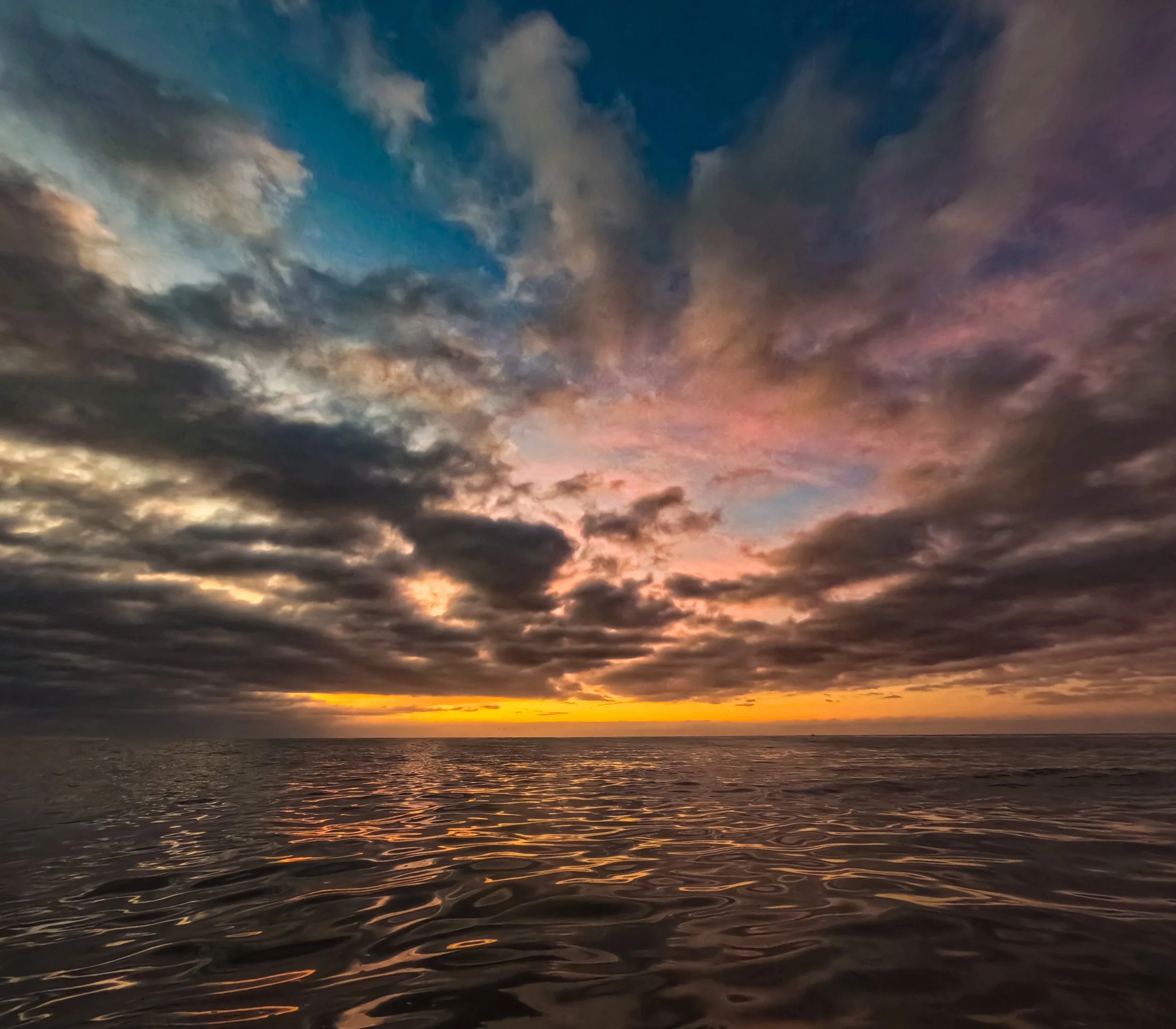 A scenic sunset over the ocean with colorful clouds in the sky and gentle waves on the water