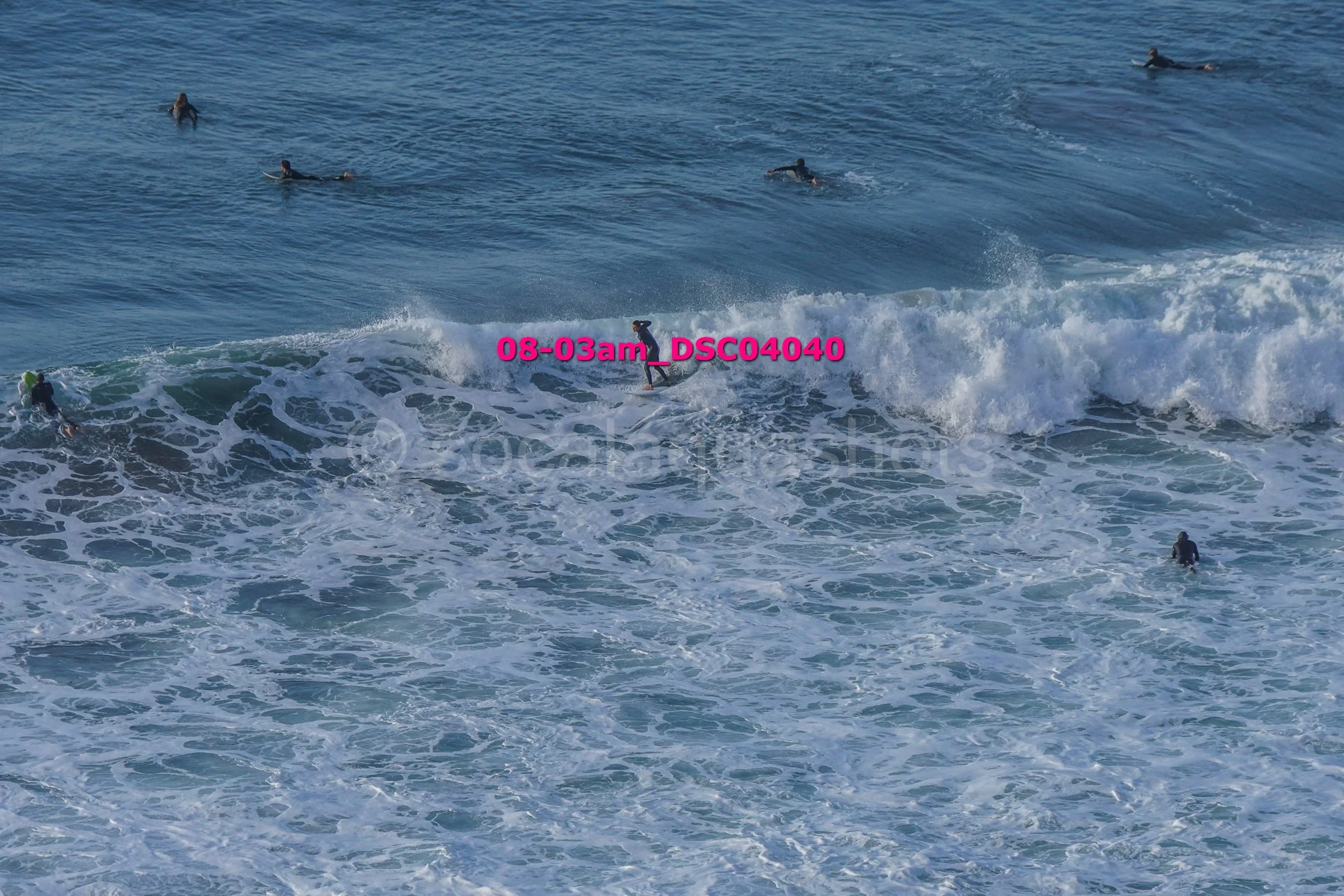 Multiple surfers riding and waiting for waves in the ocean during daylight.