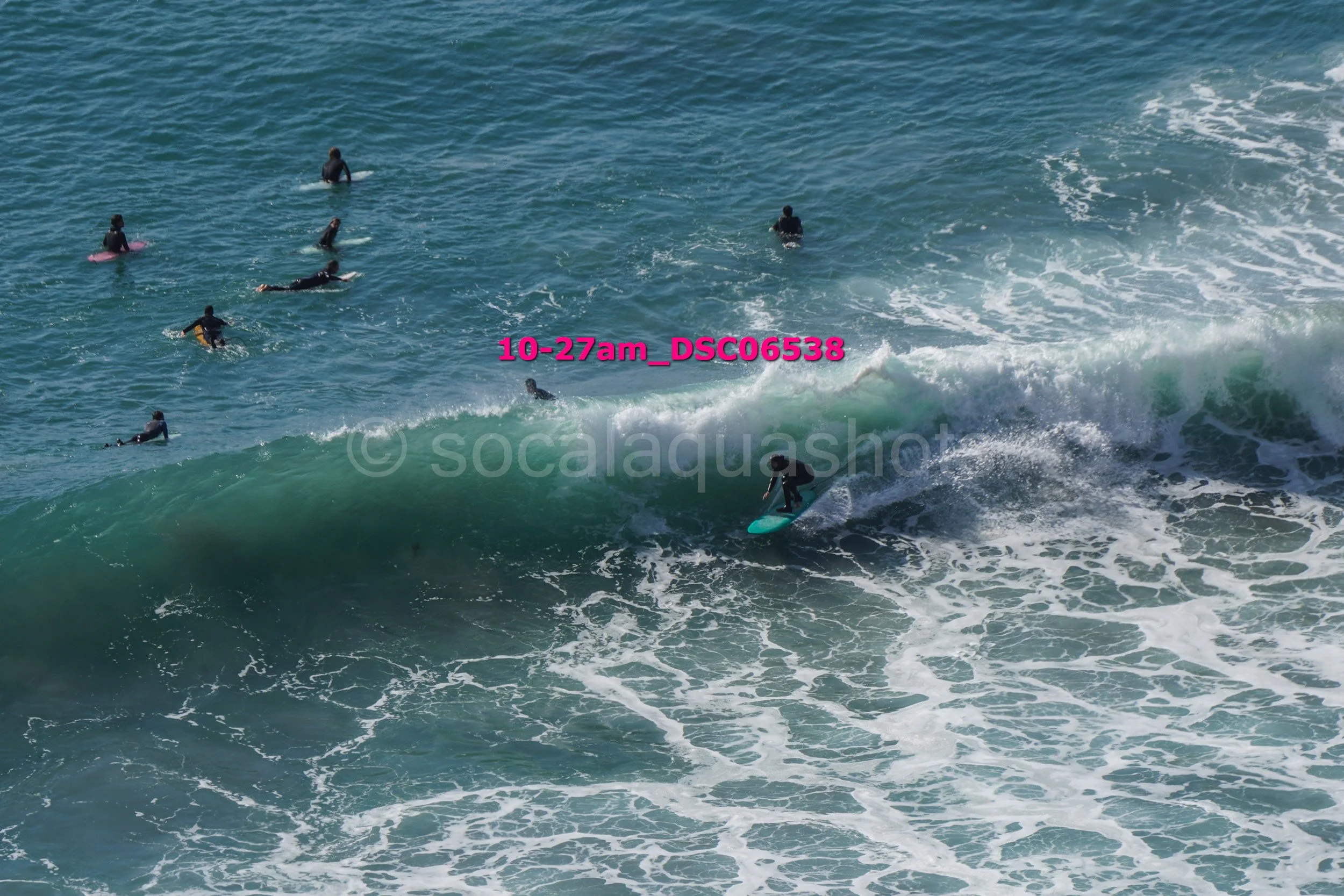 Surfer riding a wave near the shore while several people wait in the water behind him.