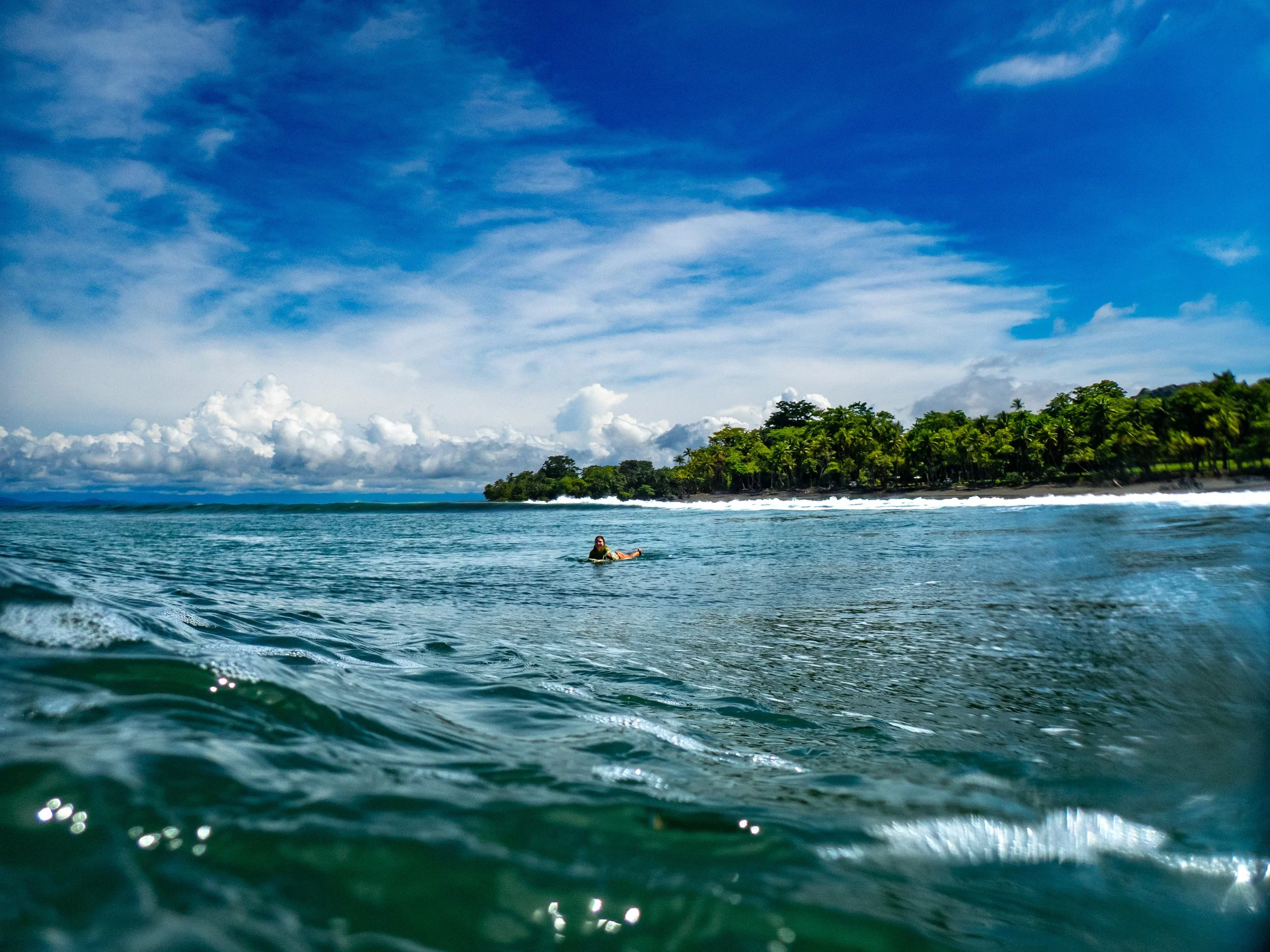 A person floating in the ocean near a tropical island with palm trees and a cloudy sky.