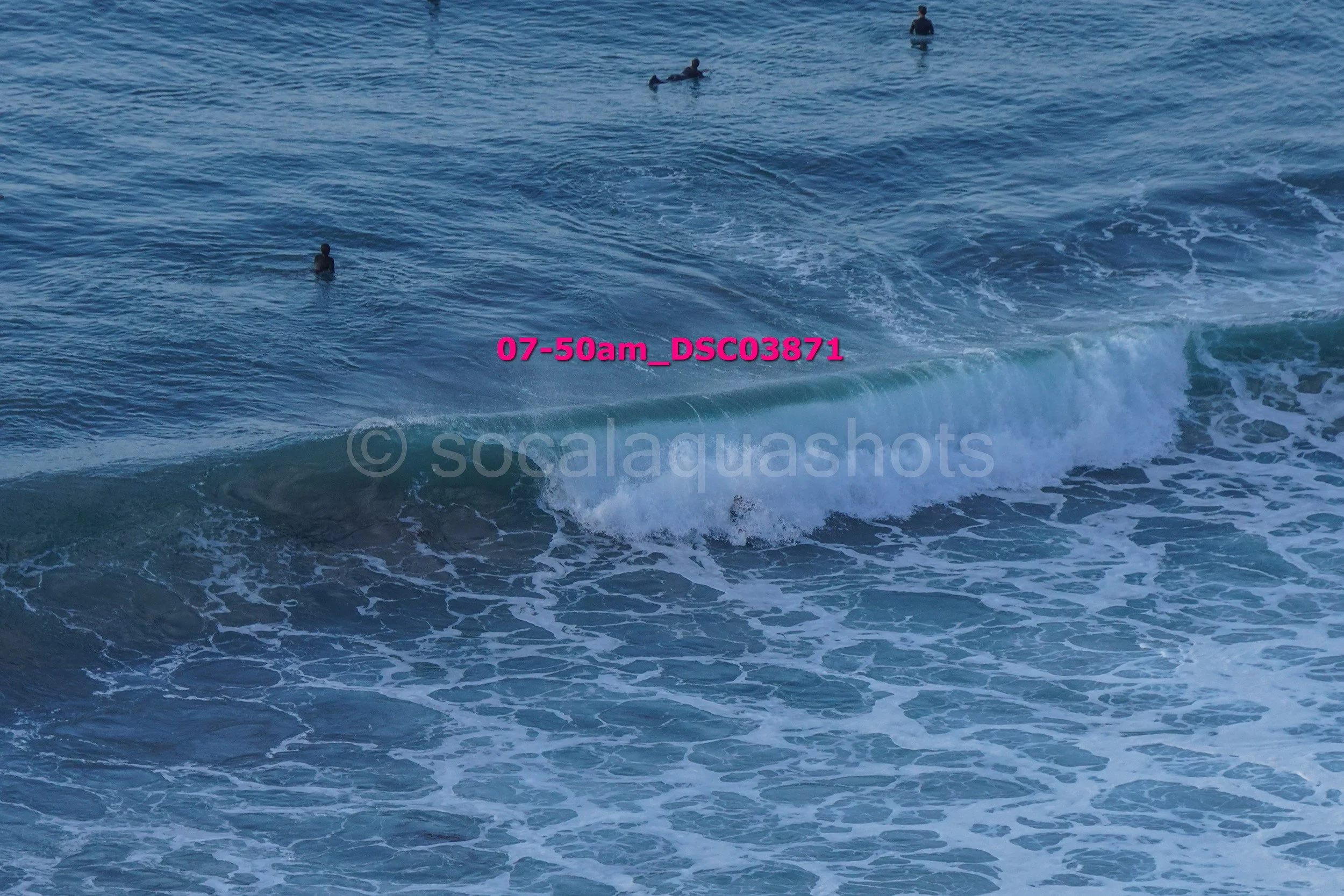 People swimming and surfing in ocean waves at a beach early in the morning.