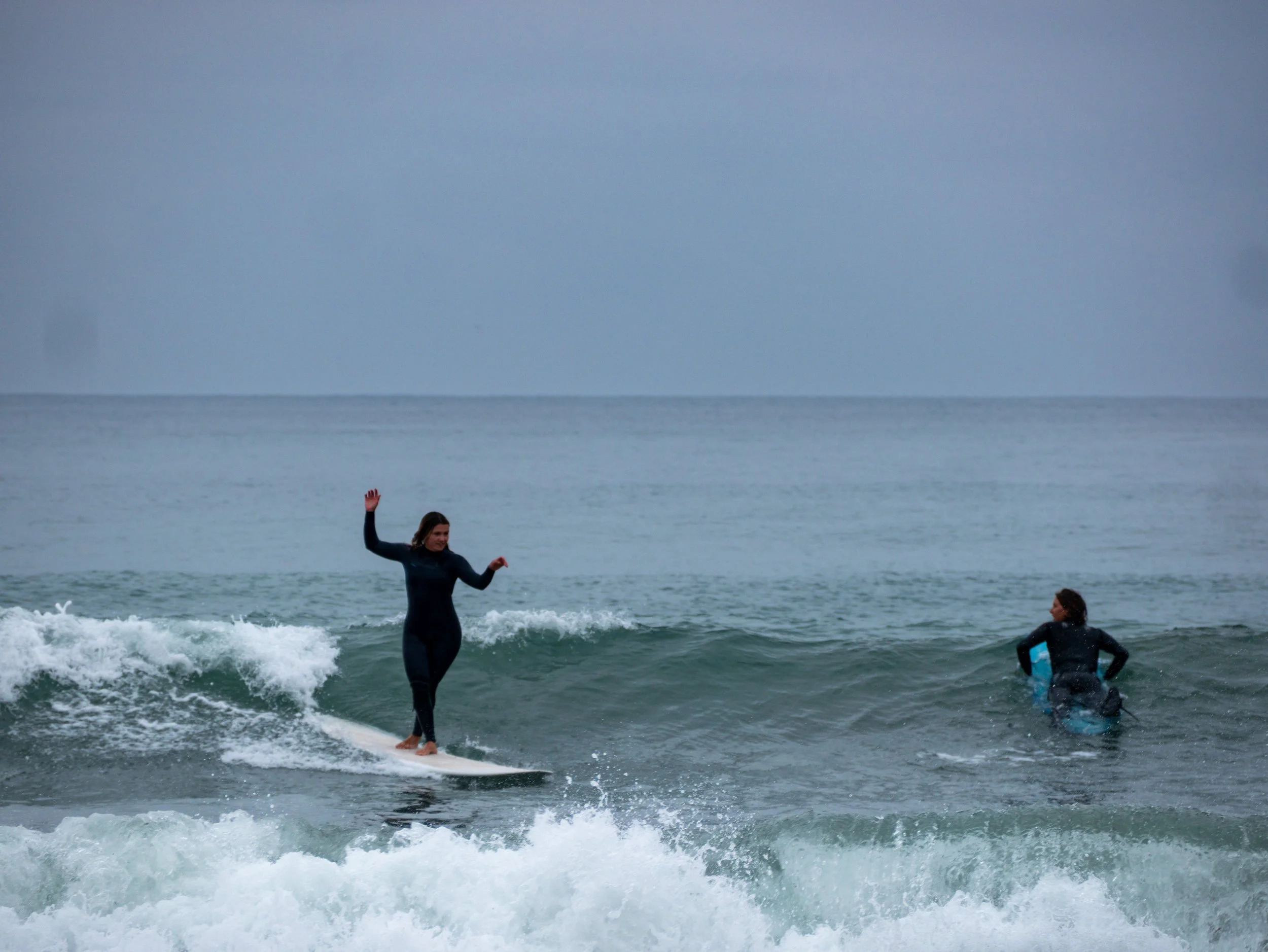 Two women surfing in the ocean on a cloudy day.