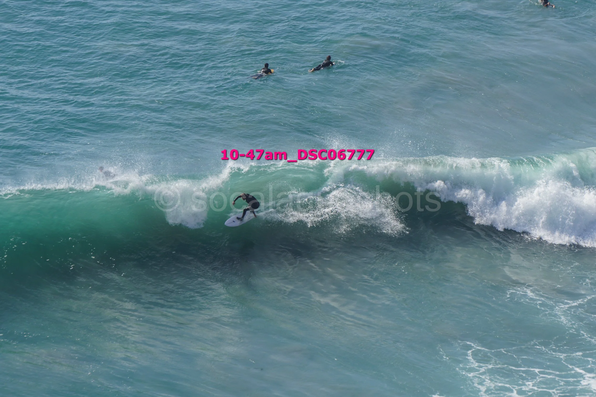 A person surfing on a large wave with three other people swimming in the water nearby.
