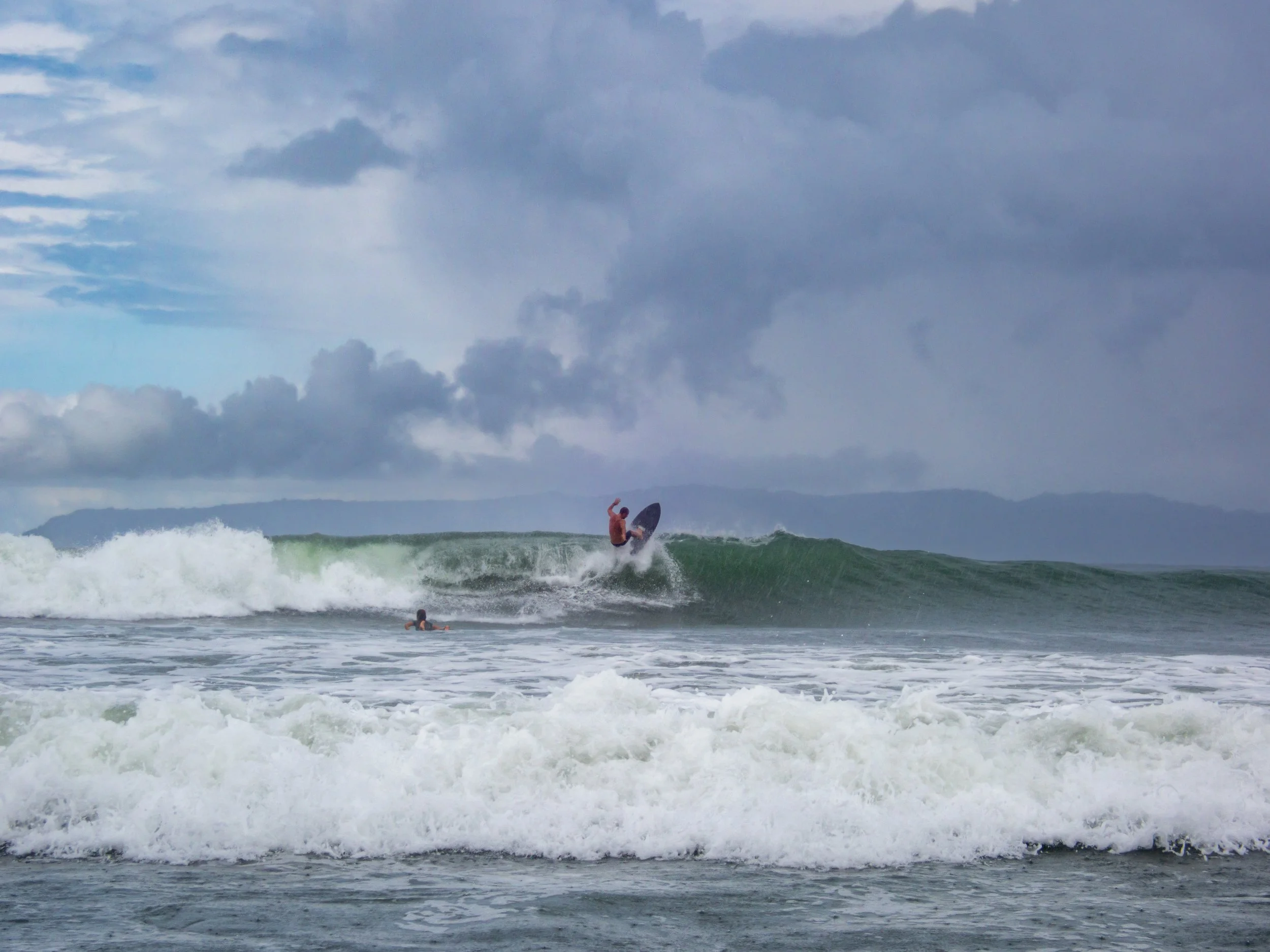 Surfer riding a large wave in the ocean with cloudy sky background