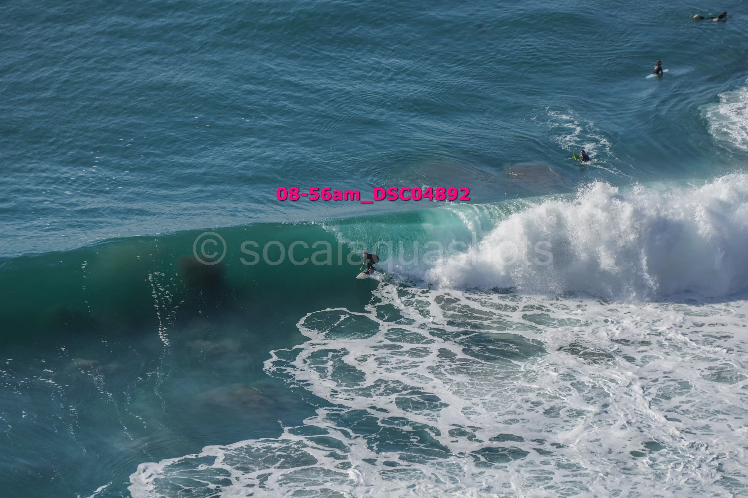 Surfer riding a wave in the ocean with several other surfers in the water nearby.