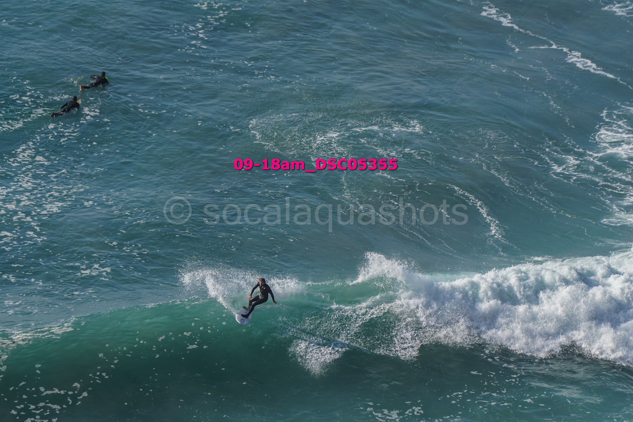 Surfer riding a wave with two surfers in the distance in the ocean.