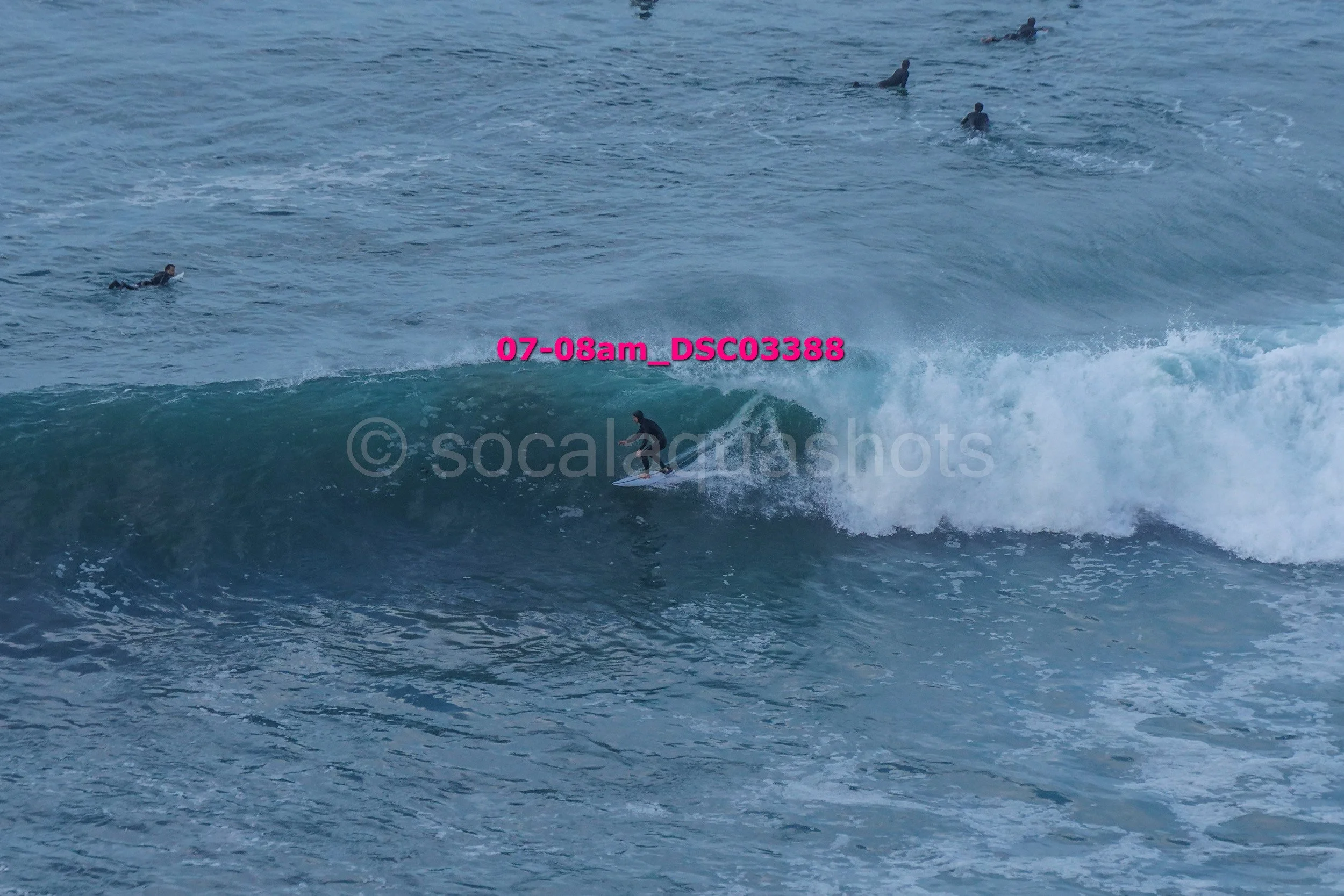 A person surfing a wave in the ocean with several people swimming or floating in the water nearby.