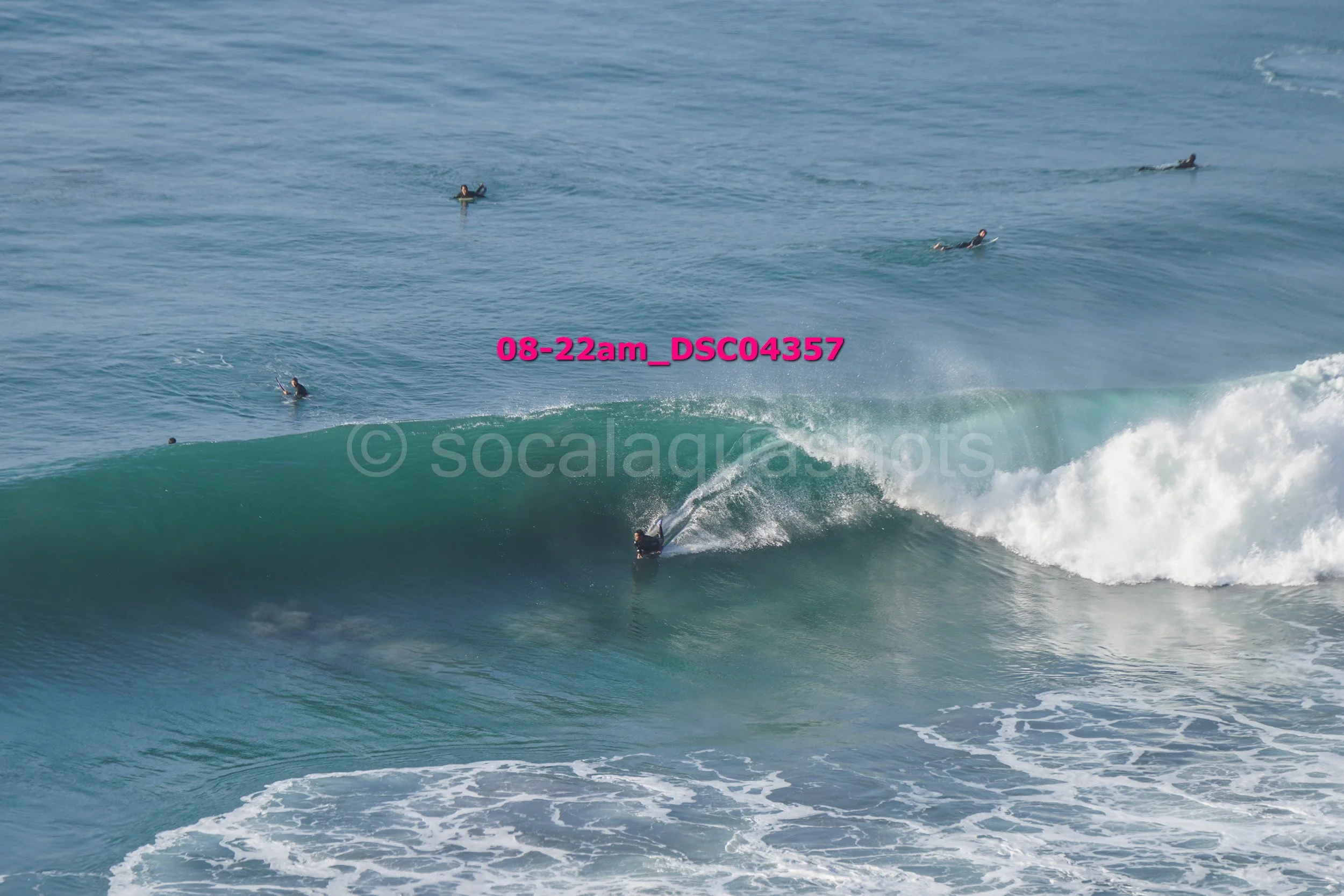 Surfer riding a large wave with several other surfers in the background in the ocean.