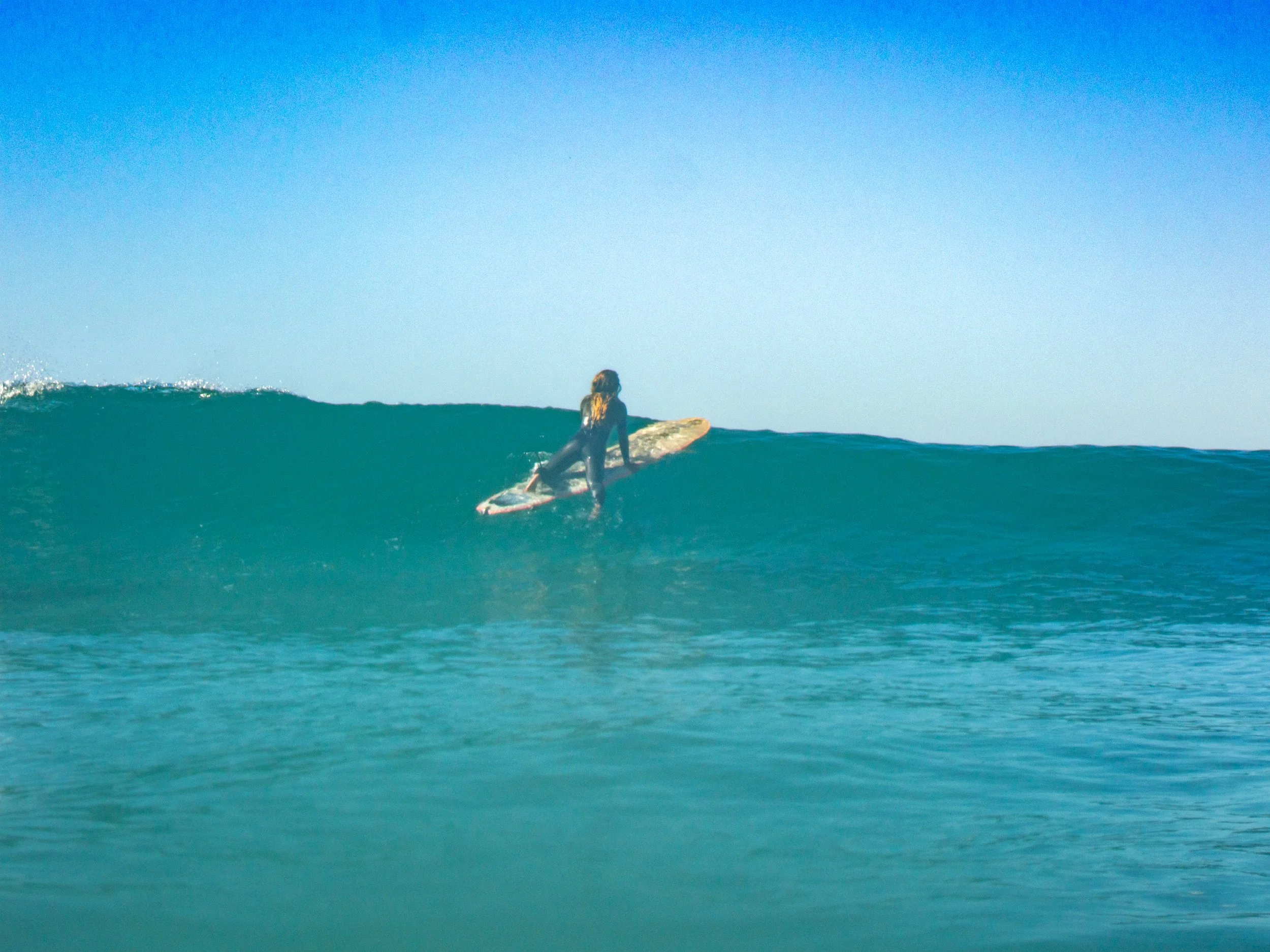 Surfer riding a wave on a clear ocean with blue sky.