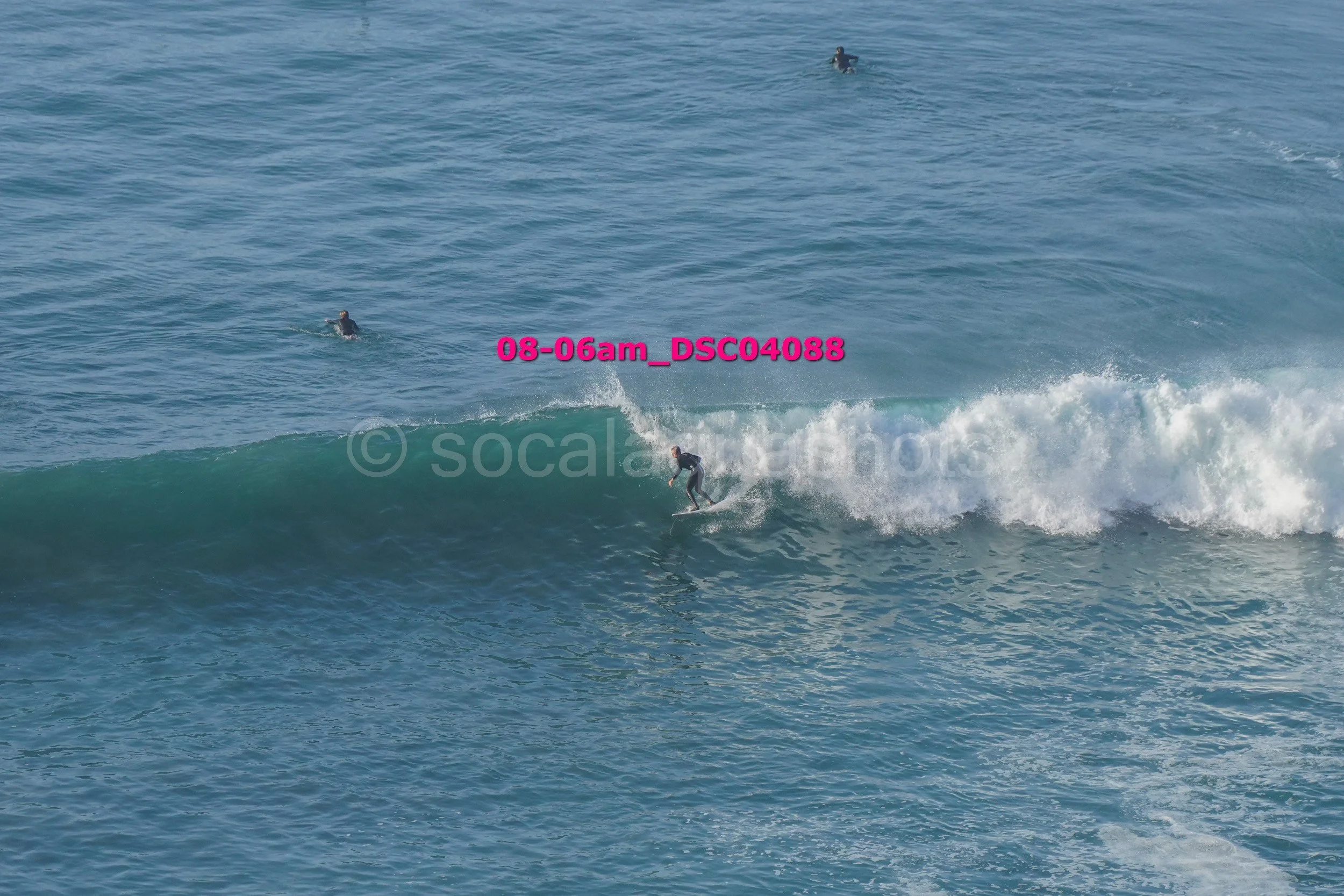 A person surfing on a wave with two other surfers visible in the water in the background in the ocean.