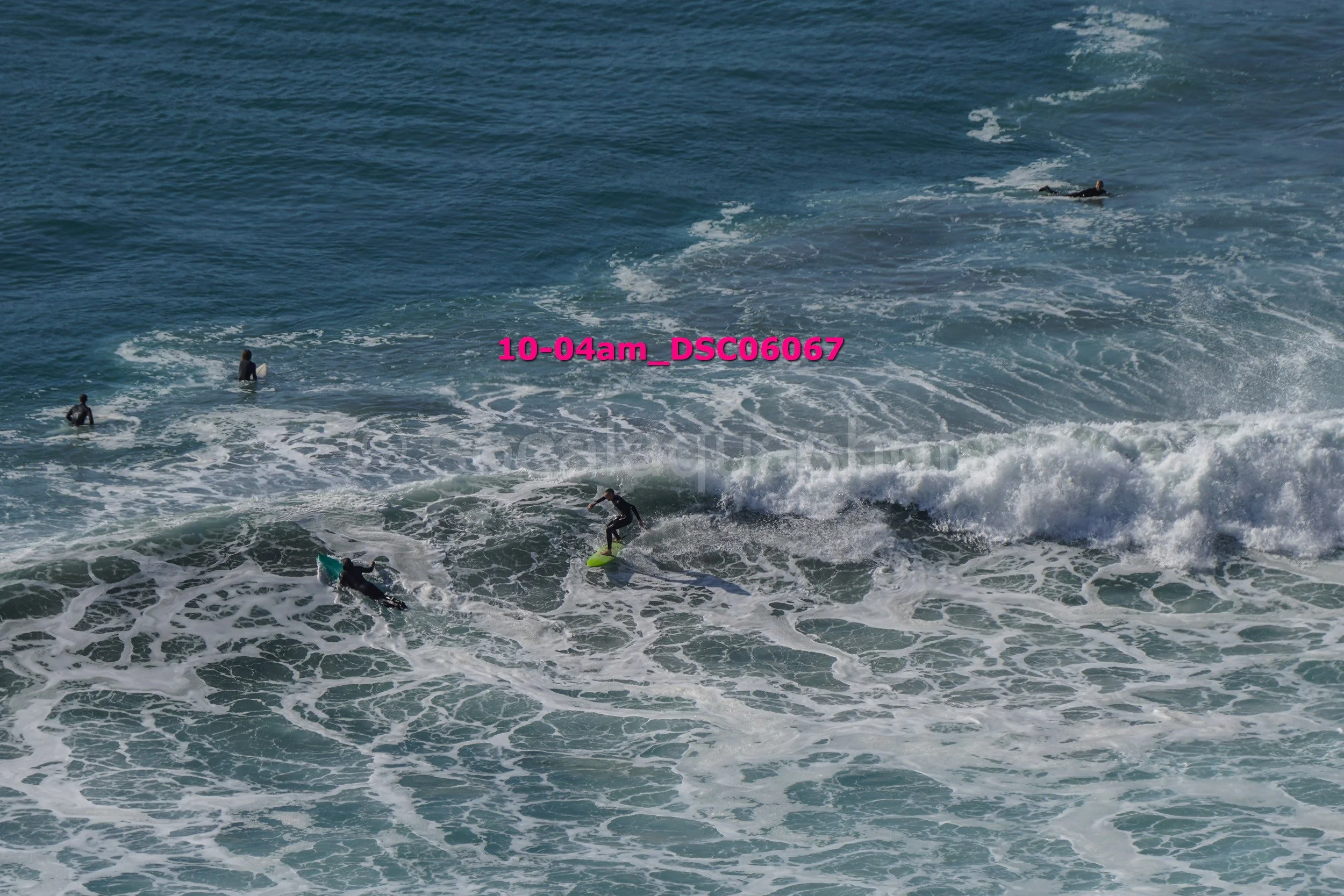 Several surfers in the ocean, some riding waves and some waiting in the water. The image captures a beach scene with surfboards and people enjoying surfing.