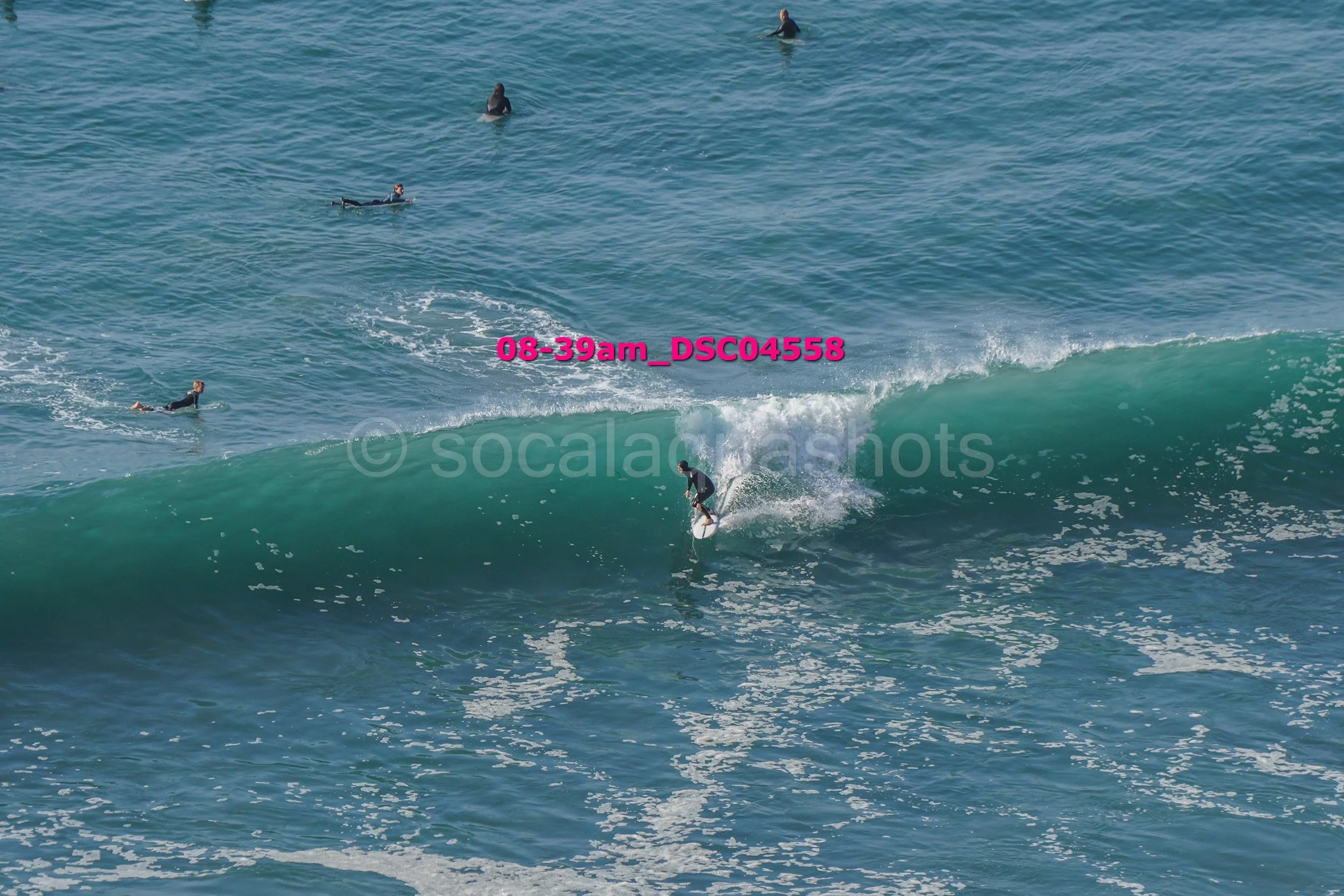 A surfer riding a wave while several people are in the water watching in the background.