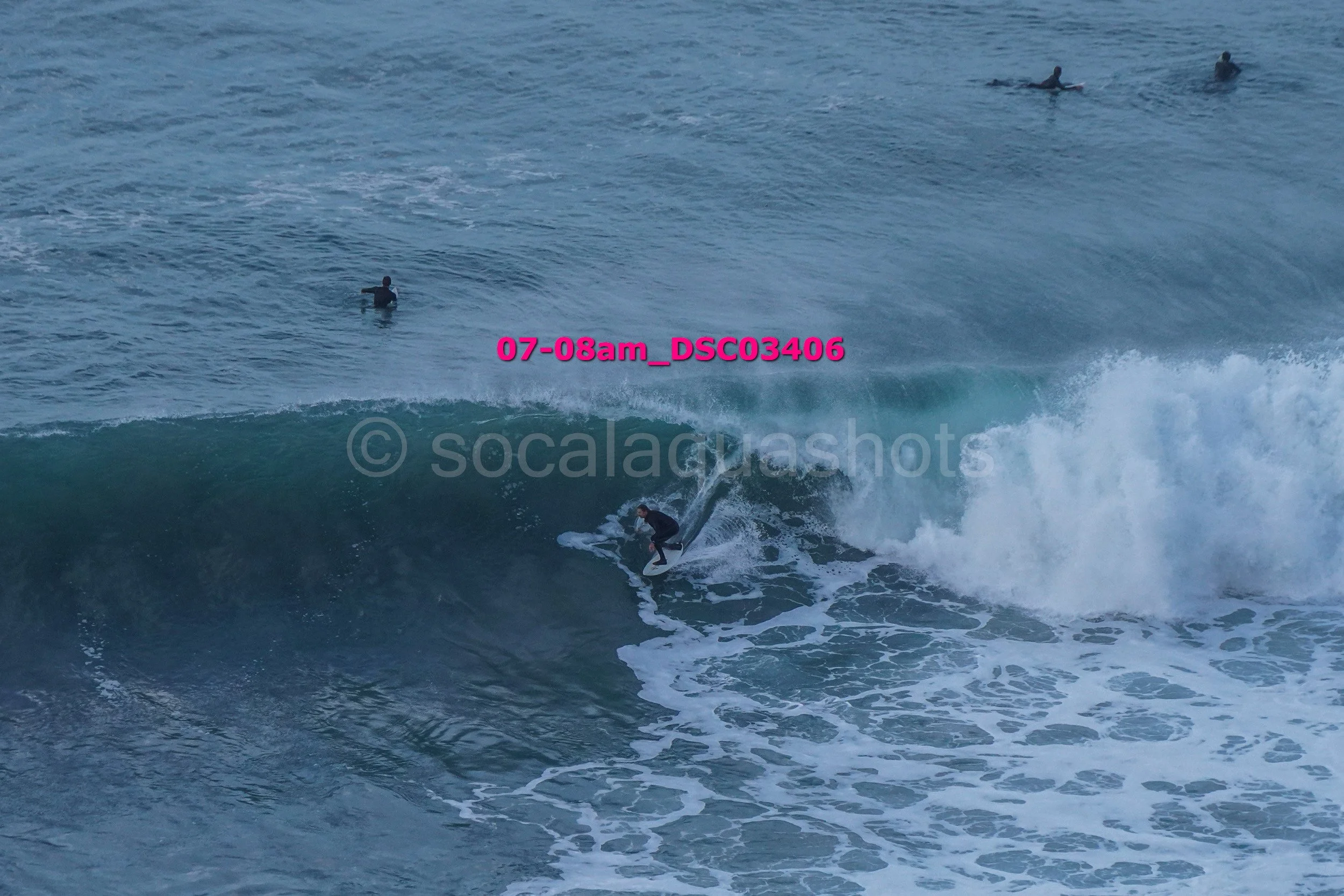 A person surfing a large wave in the ocean, with several other people on surfboards farther out