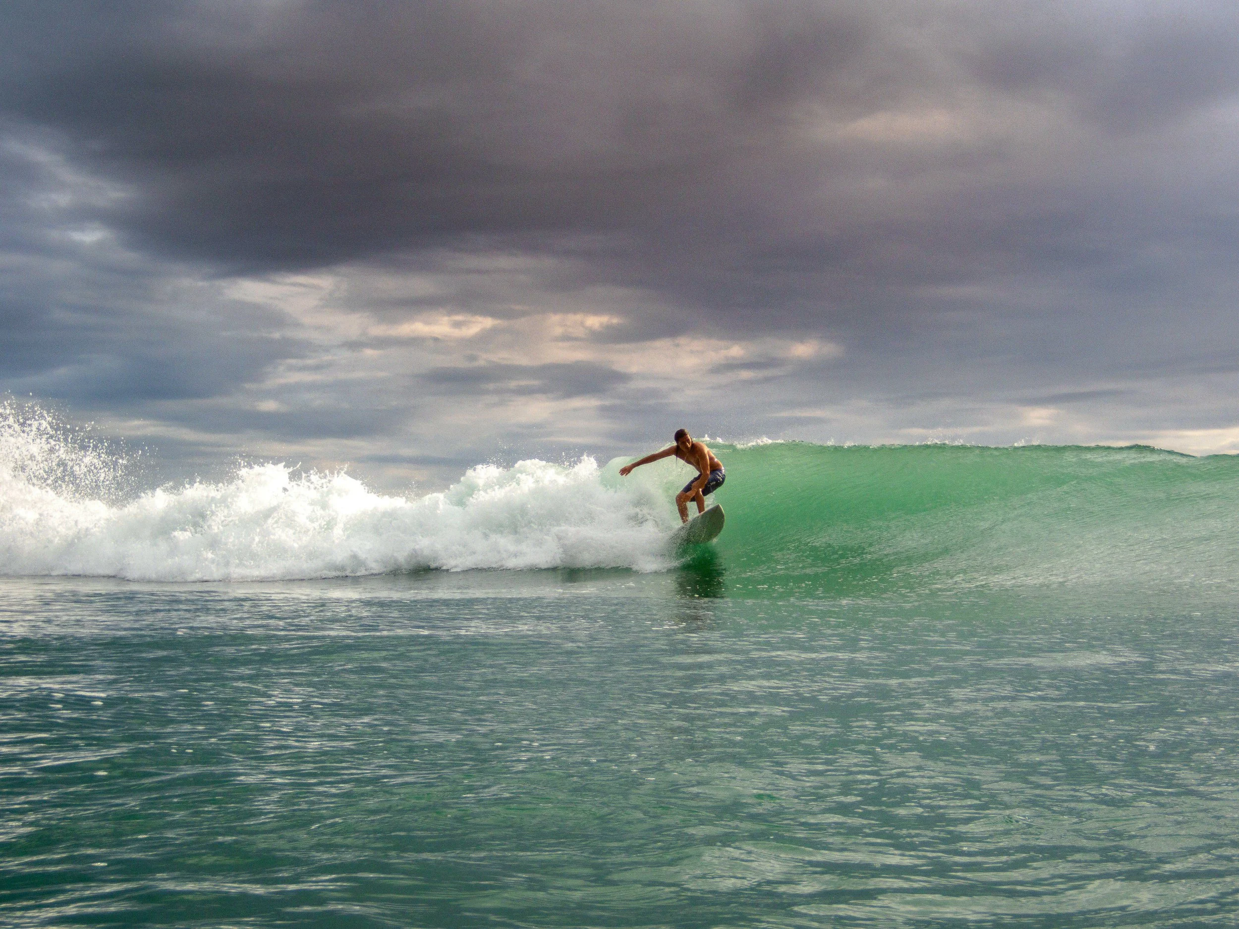 Surfer riding a wave under cloudy sky.