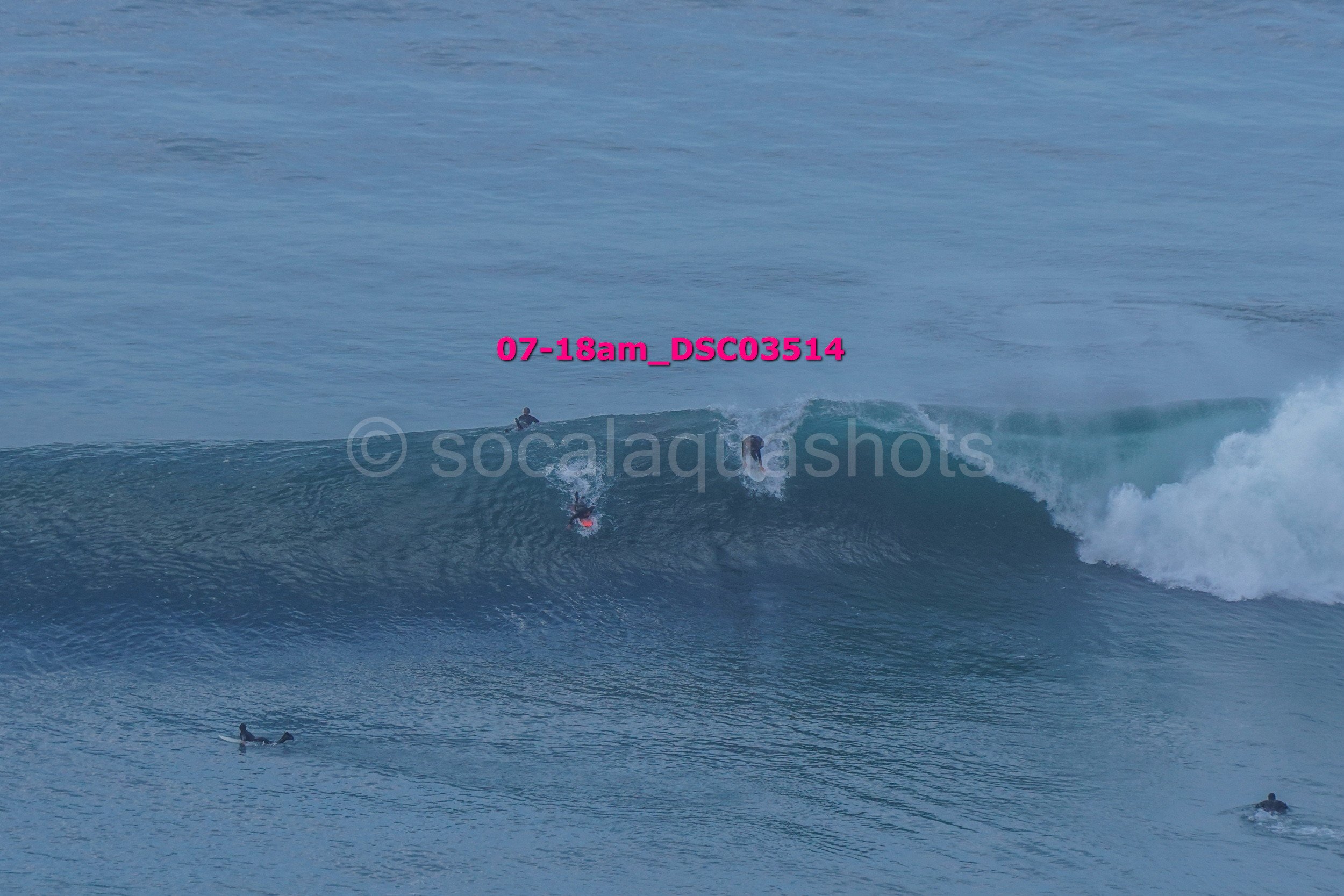 Surfers riding a large wave in the ocean during daylight with several other surfers in the water.