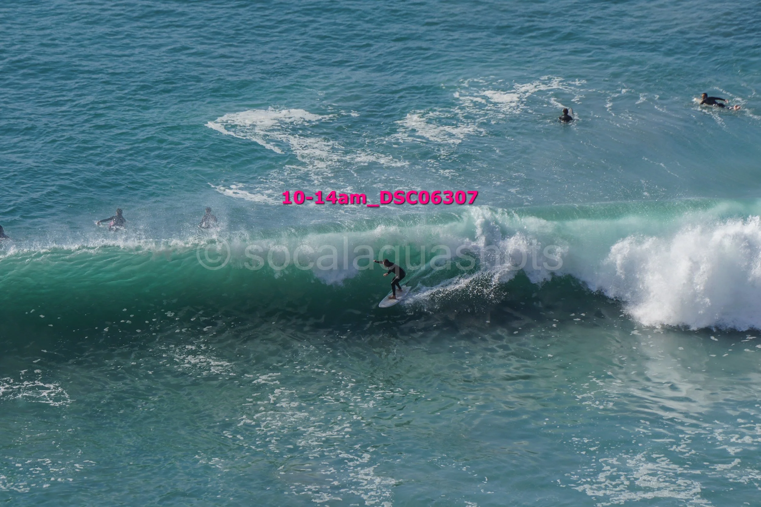 Surfer riding a wave in the ocean with other surfers in the water.