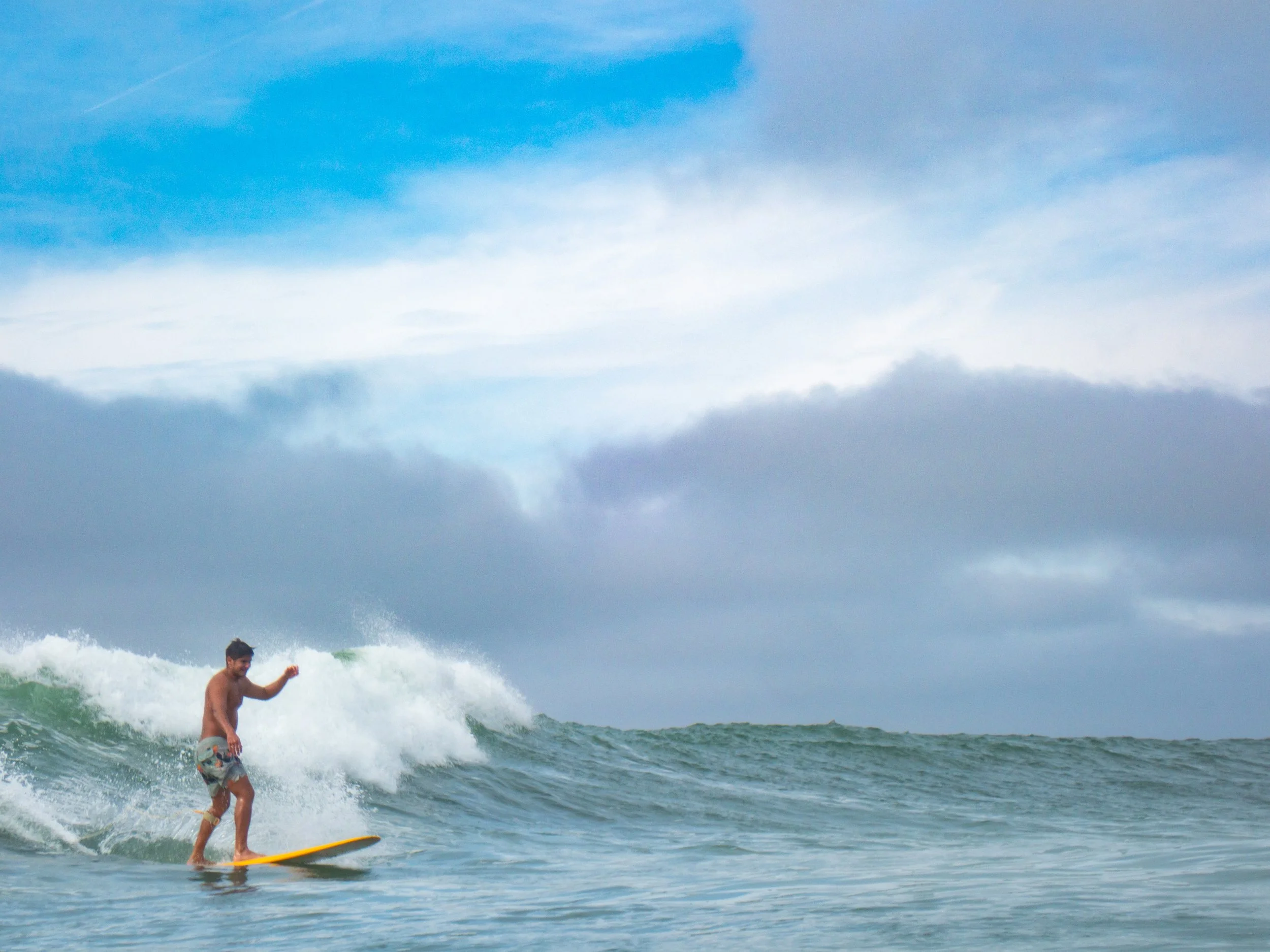 A man surfing on a yellow surfboard in the ocean, with cloudy sky above.