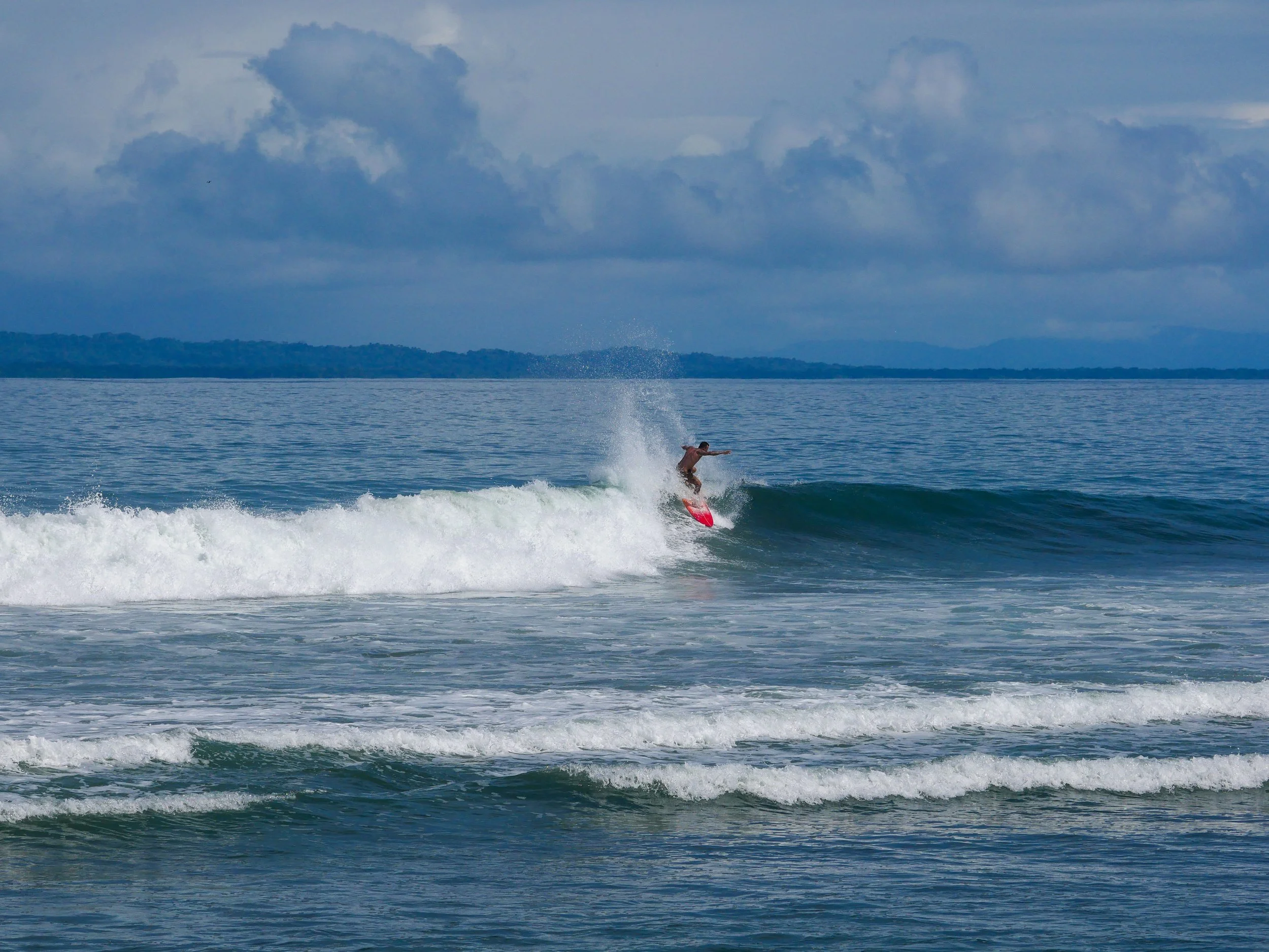 Surfer riding a wave on a red surfboard under cloudy skies