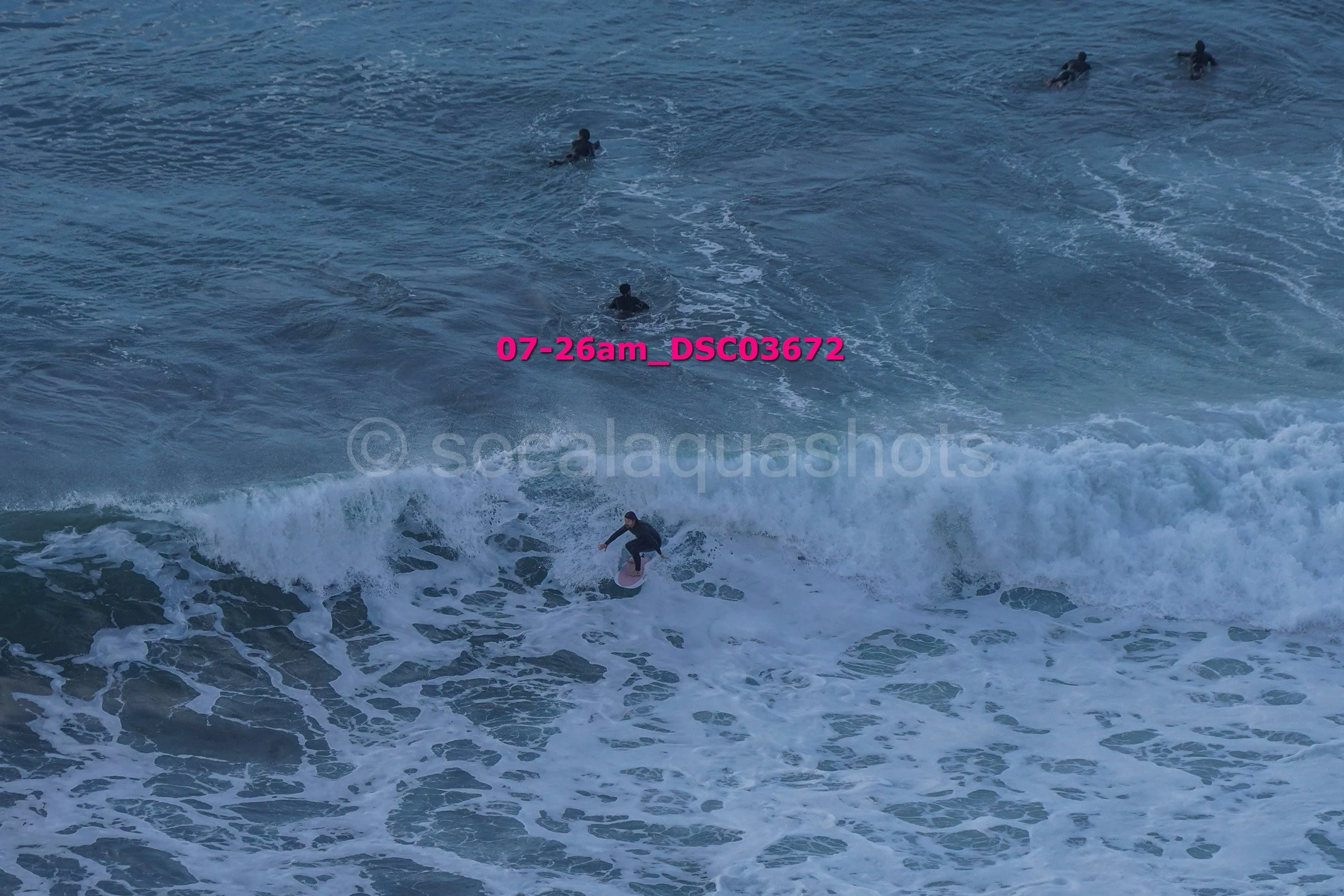 Surfer riding a wave while other surfers float in the water nearby on the ocean.