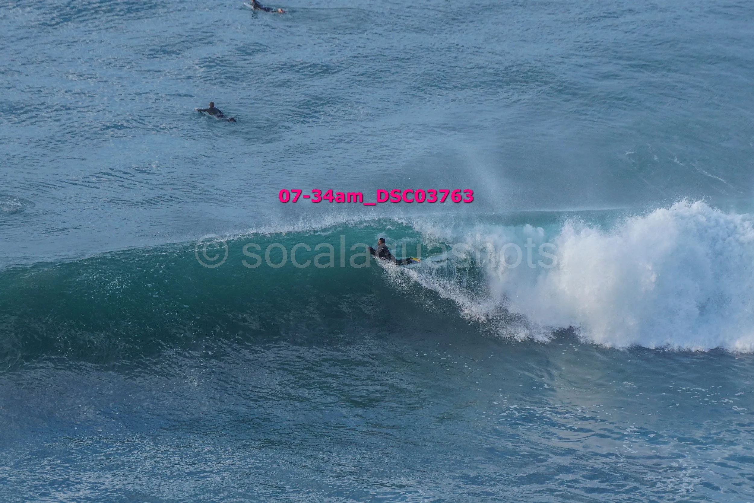 A surfer catching a wave with another person swimming in the background in the ocean.
