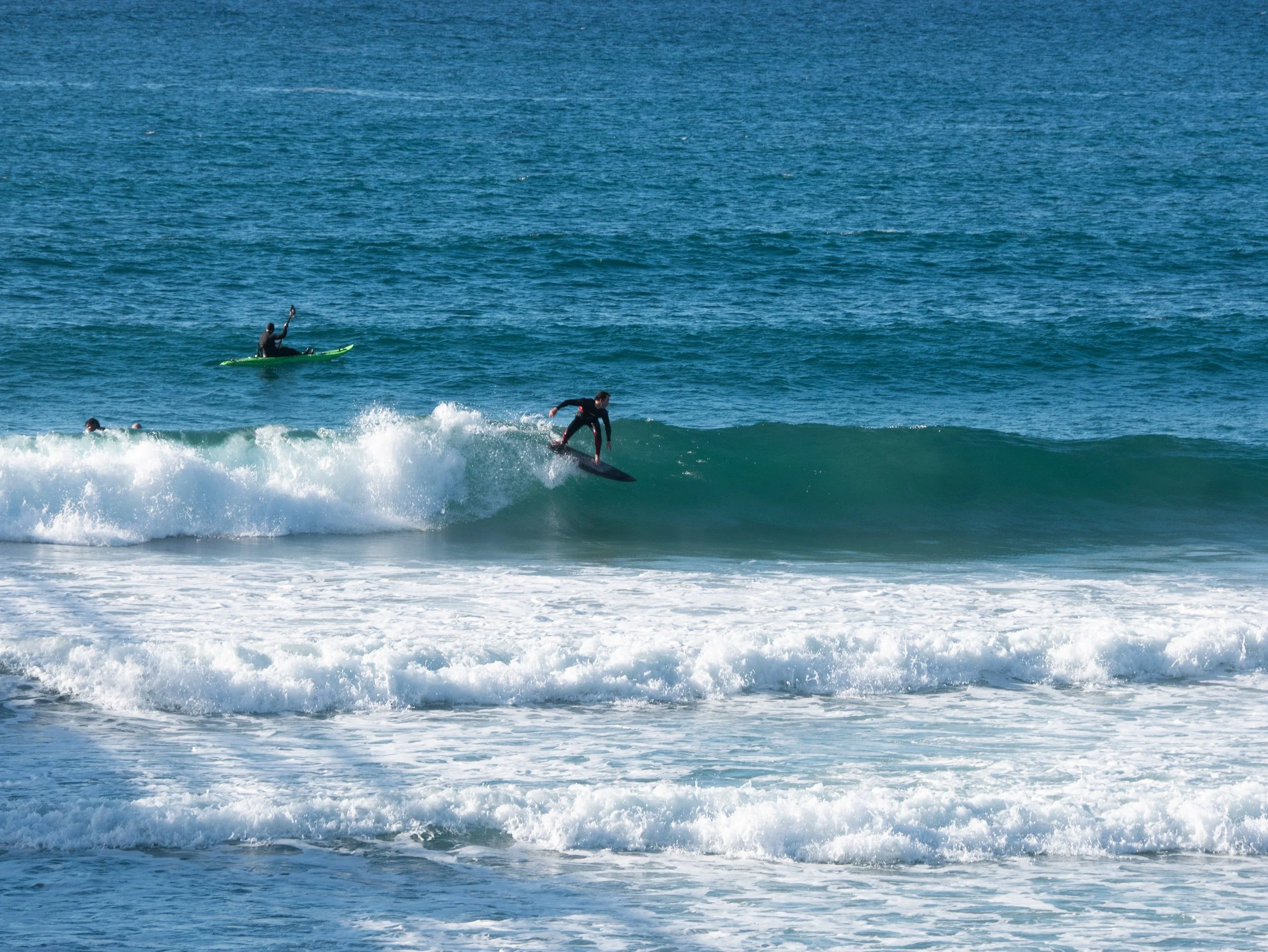 Person surfing on a wave in the ocean, with a person on a paddleboard in the background